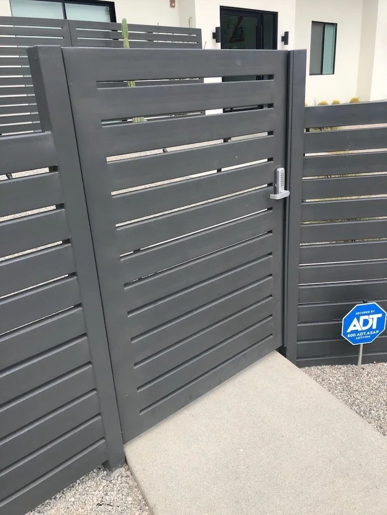 dark grey slat gate with adjacent matching fence panels and a silver handle at the front of a home