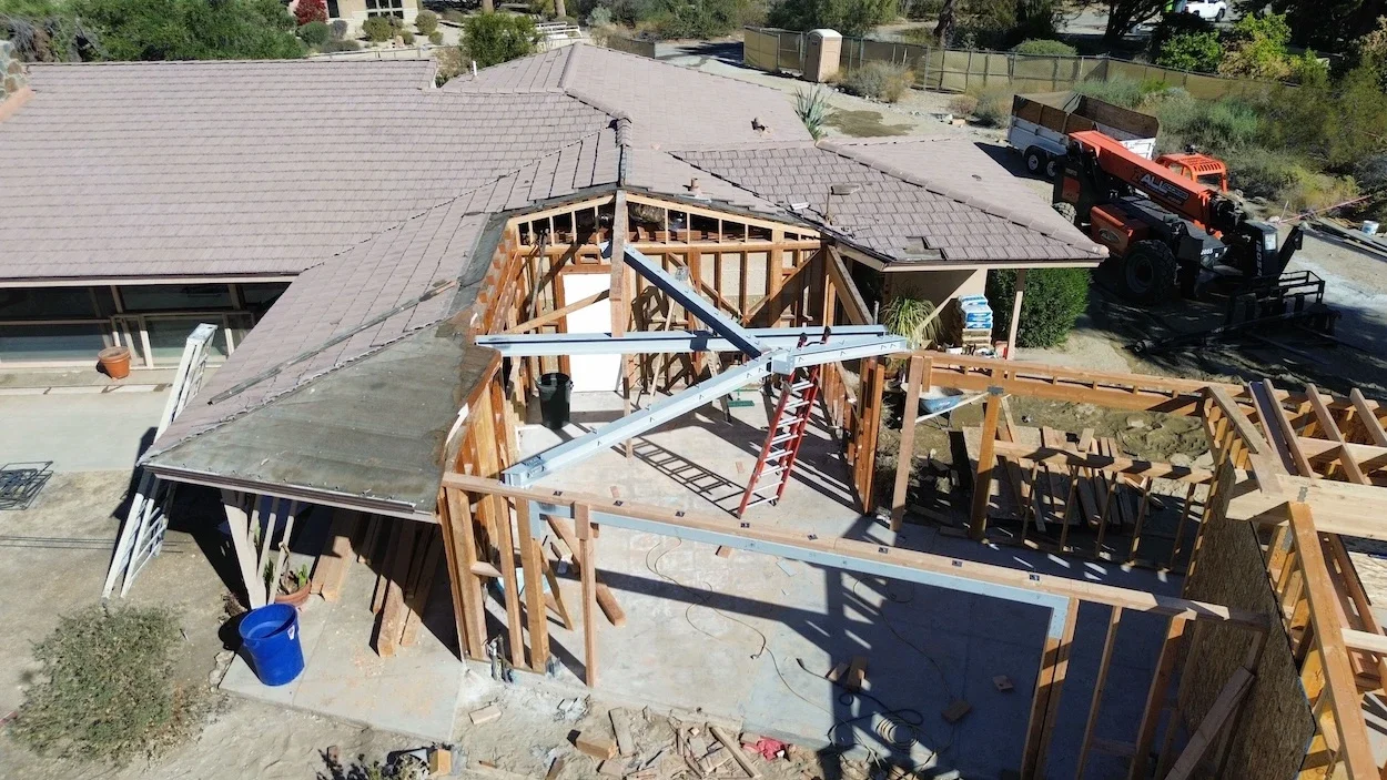 aerial view of a home under construction with an exposed roof and new intersecting structural steel beams