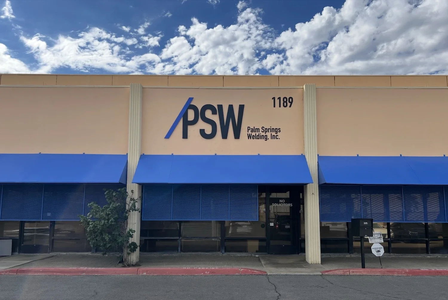 a tan building with blue awnings and metal sun screens and a sign that says PSW, Palm Springs Welding, Inc., and 1189