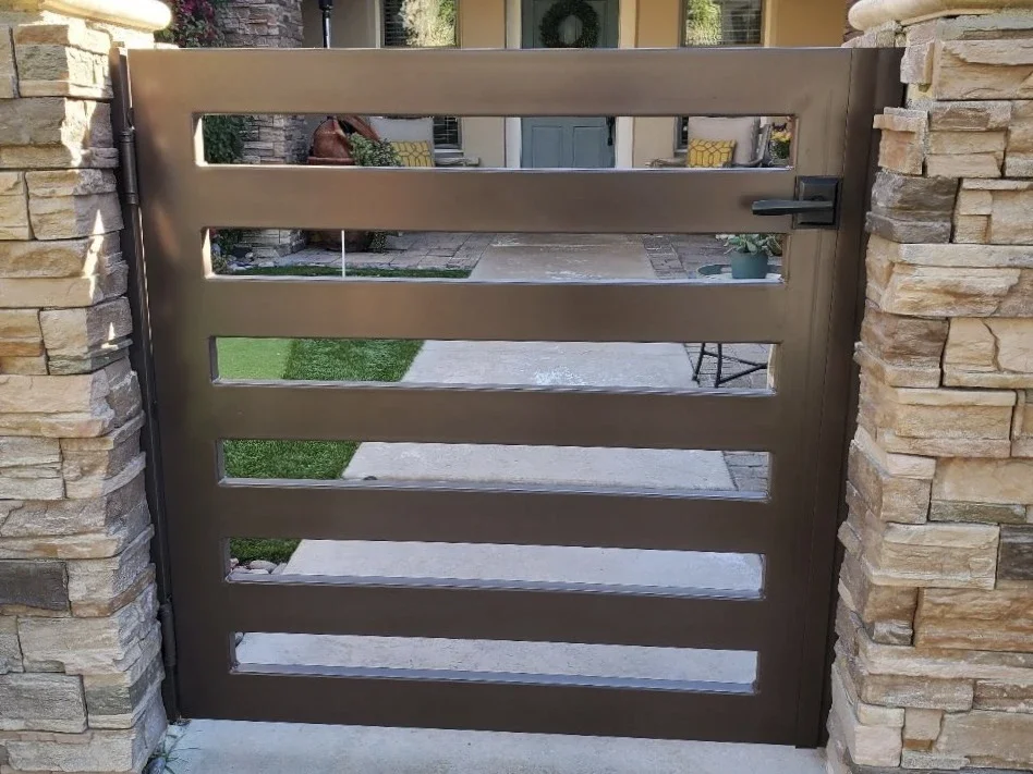 shiny dark gold slat gate attached to stone pillars leading into a home’s front courtyard