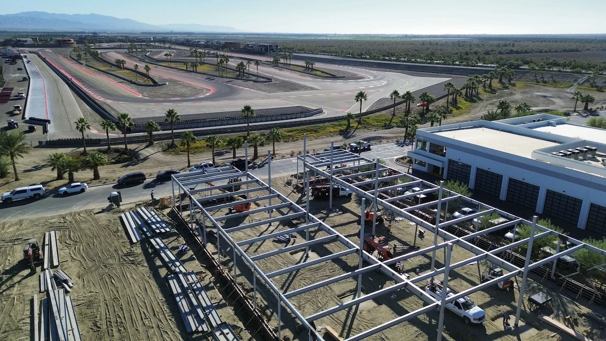 large structural steel project consisting of two parallel rectangular structures made of columns and beams with a racetrack and palm trees behind it