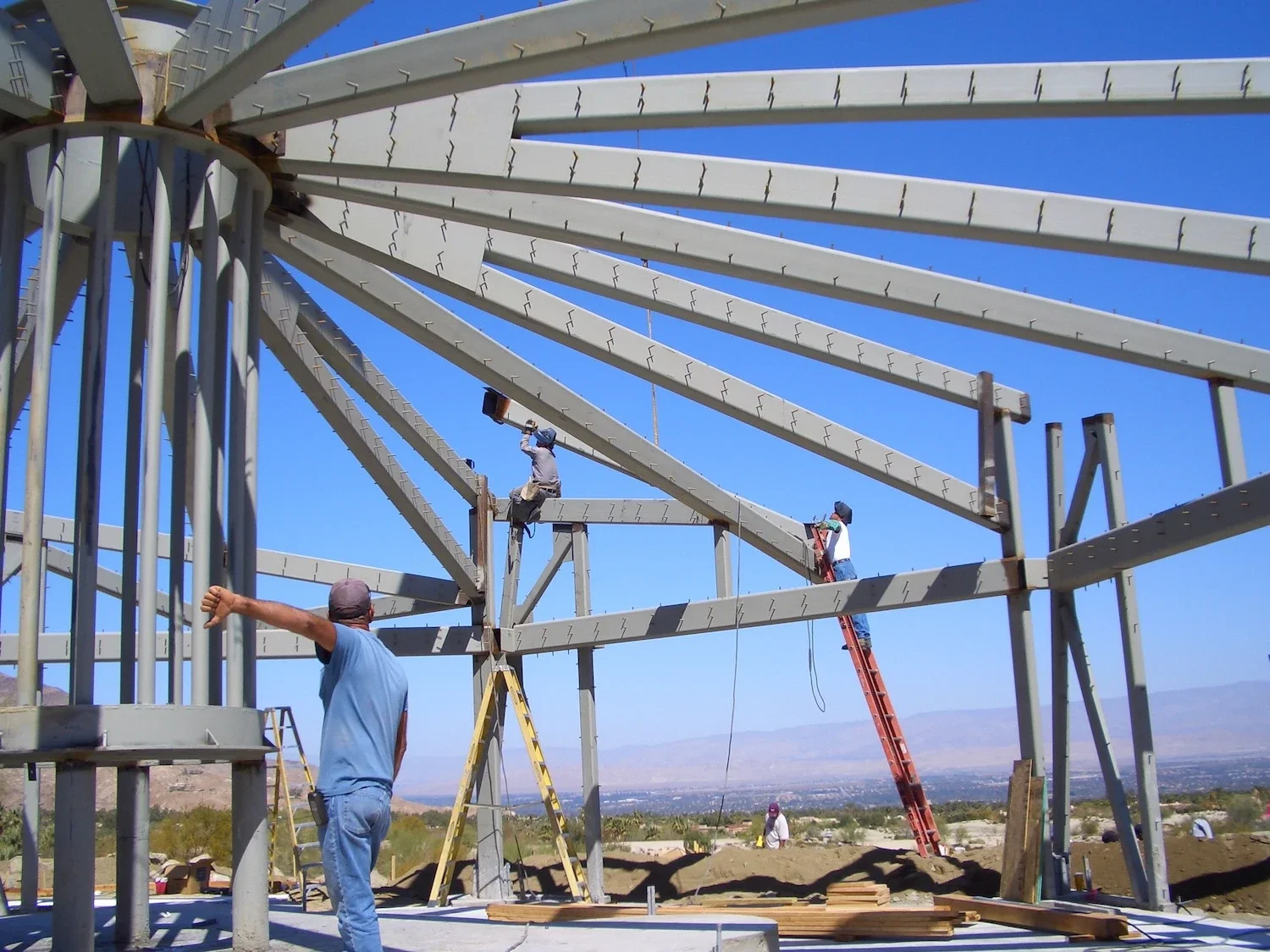 a collection of beams forming a tube-like structure with connected roof beams that slant down from the top being installed on a jobsite