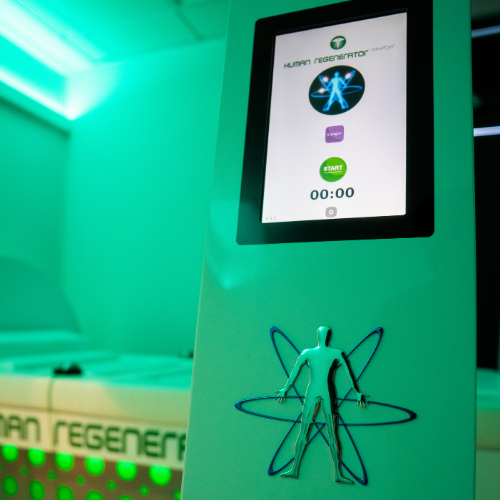Touchscreen kiosk with a fitness app and a decorative wire figure of a human on its lower part, in a room with green illumination.