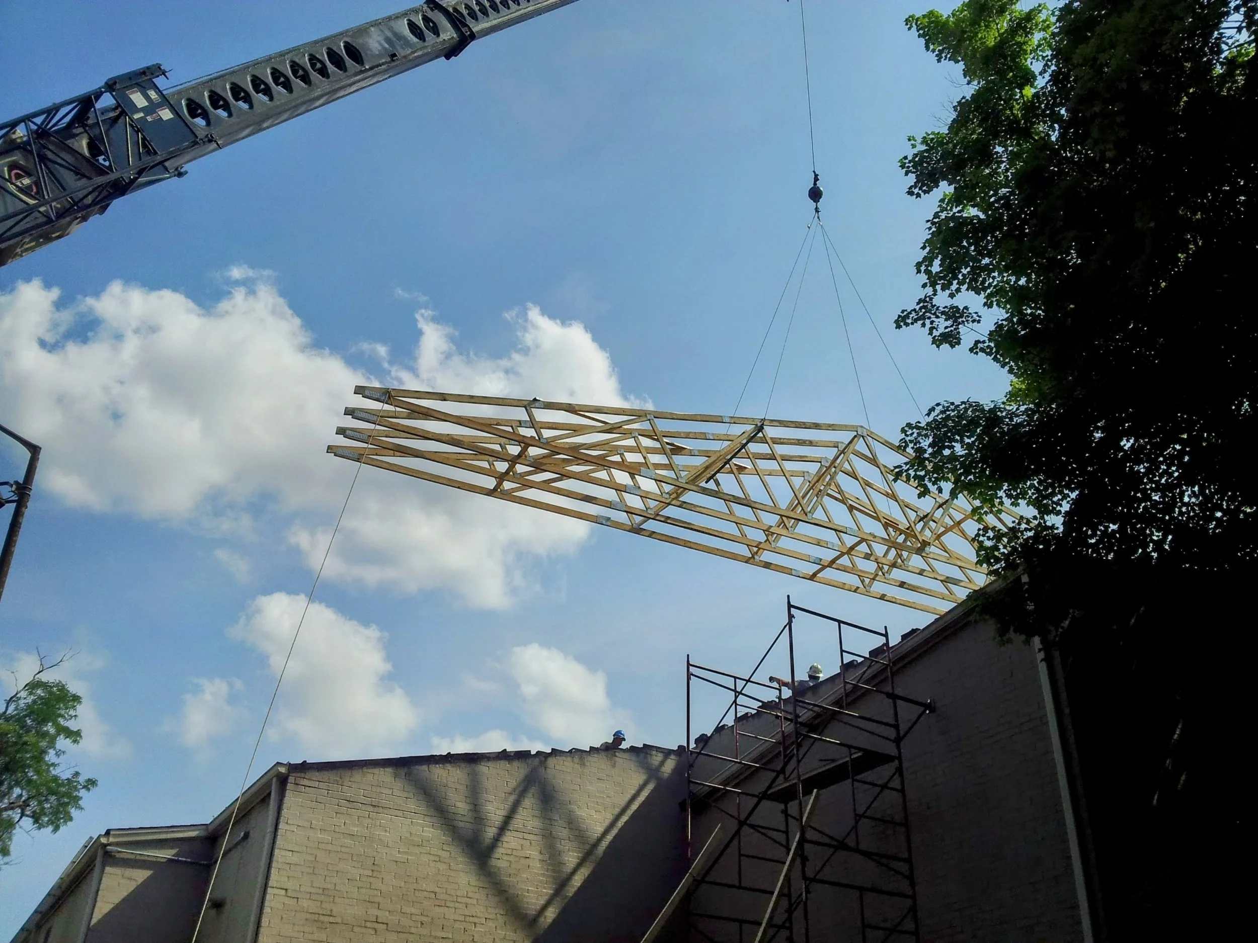 Crane lifting a wooden construction frame above a building under construction, with scaffolding and workers on the roof.