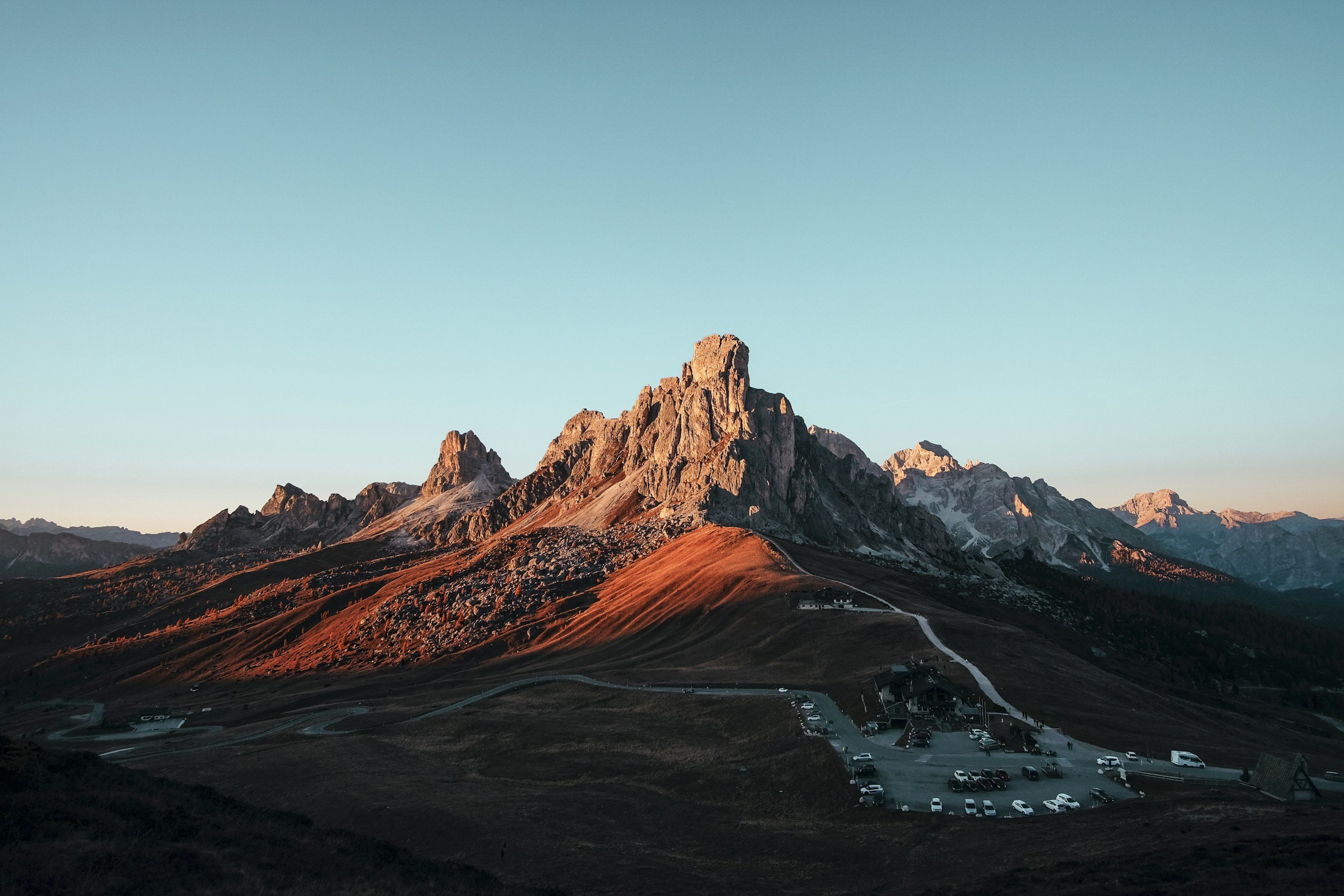 Mountain landscape during sunset with rocky peaks and parking lot at the base.