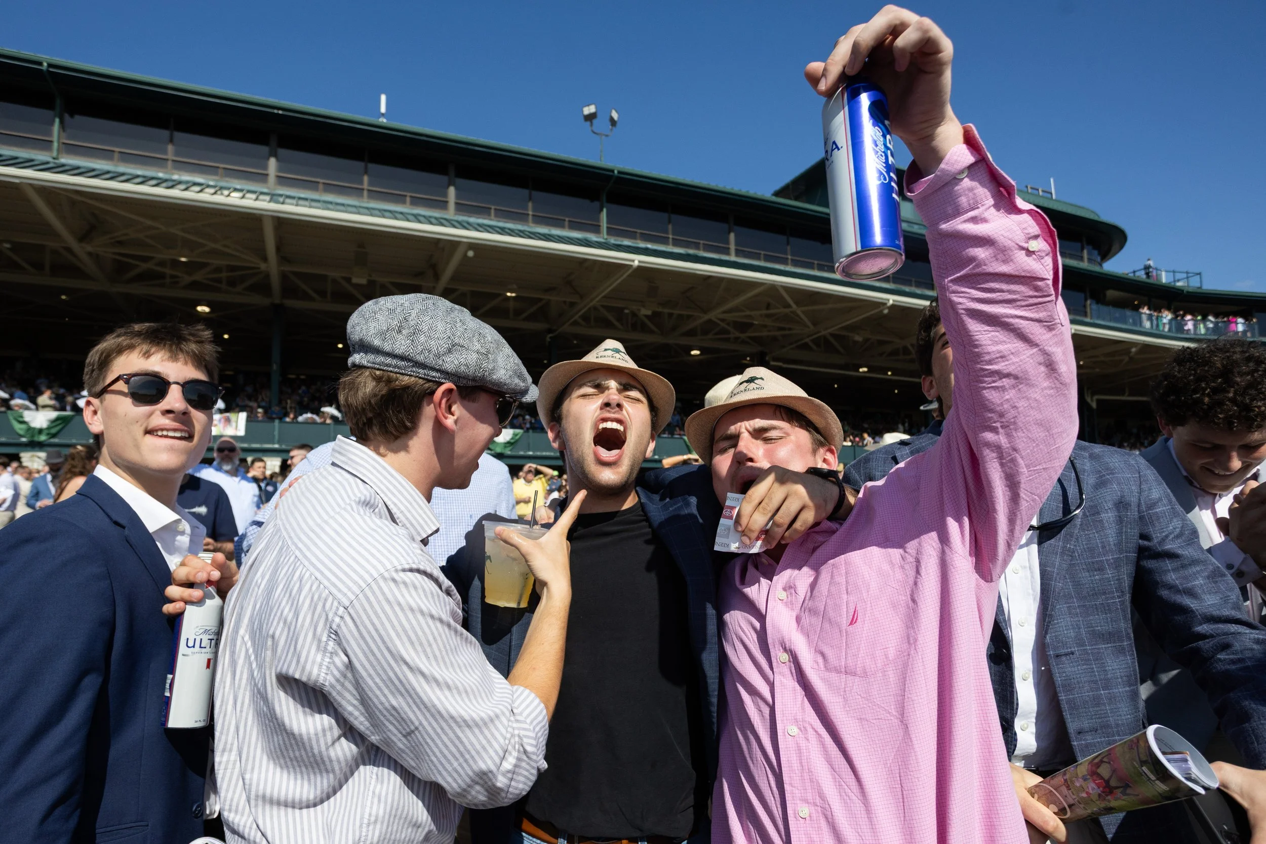 Group of men at a sporting event celebrating, with one man holding up a can of Red Bull energy drink.