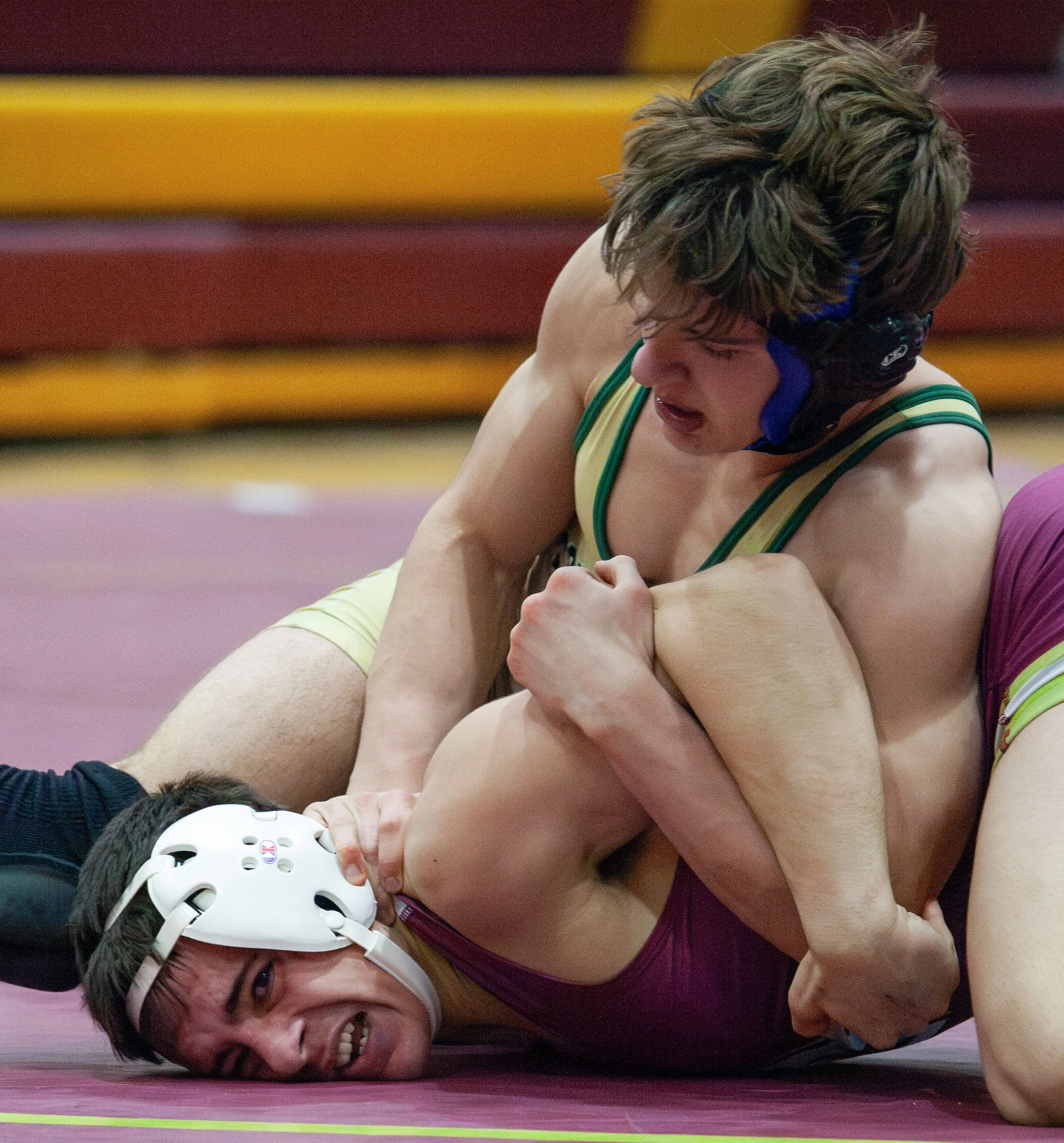 Two female wrestlers engaged in a match on a pink wrestling mat, with intense expressions and physical contact.