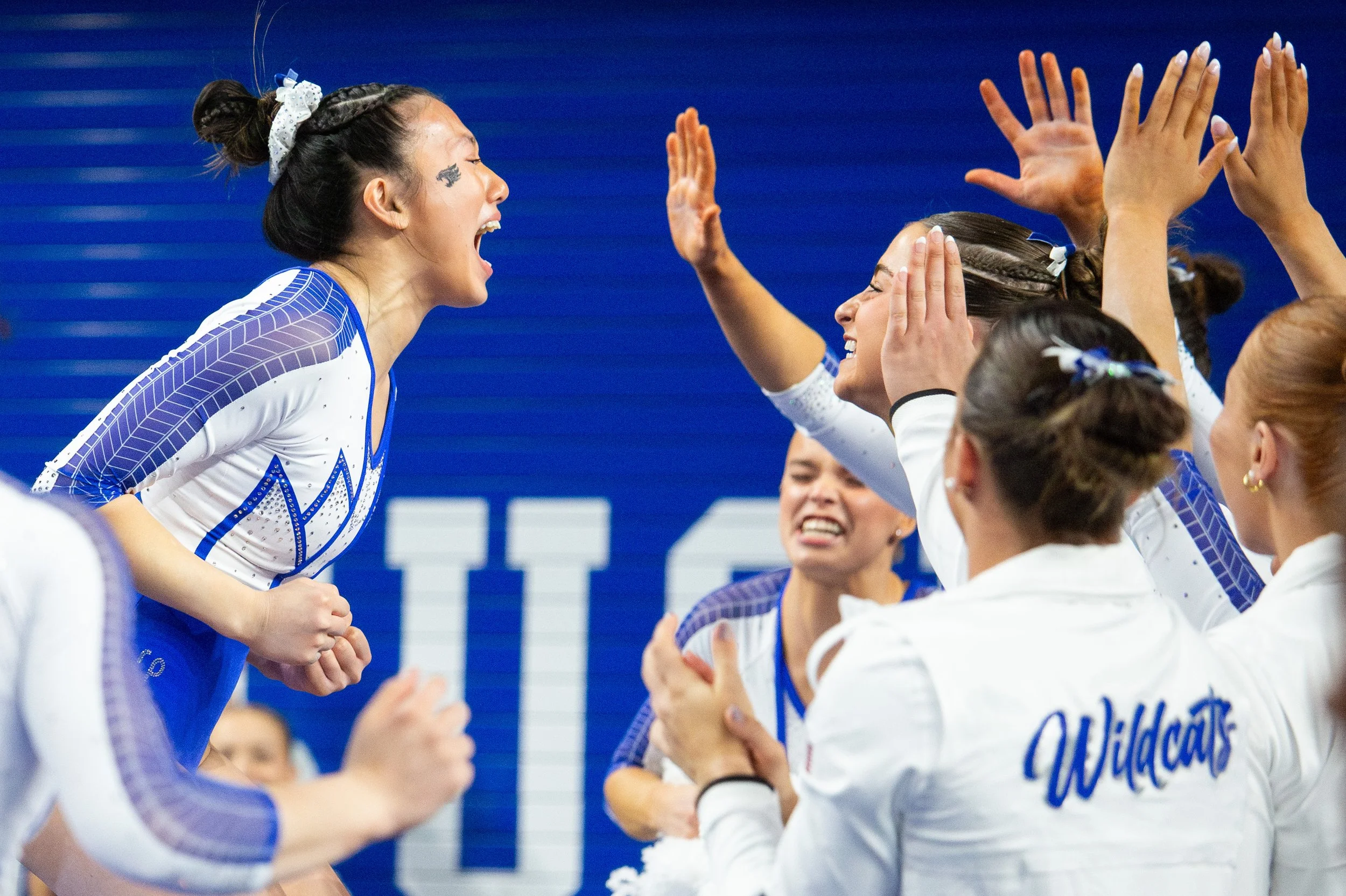 Group of female volleyball players celebrating on the court, with one player in the foreground shouting and others clapping and raising hands.