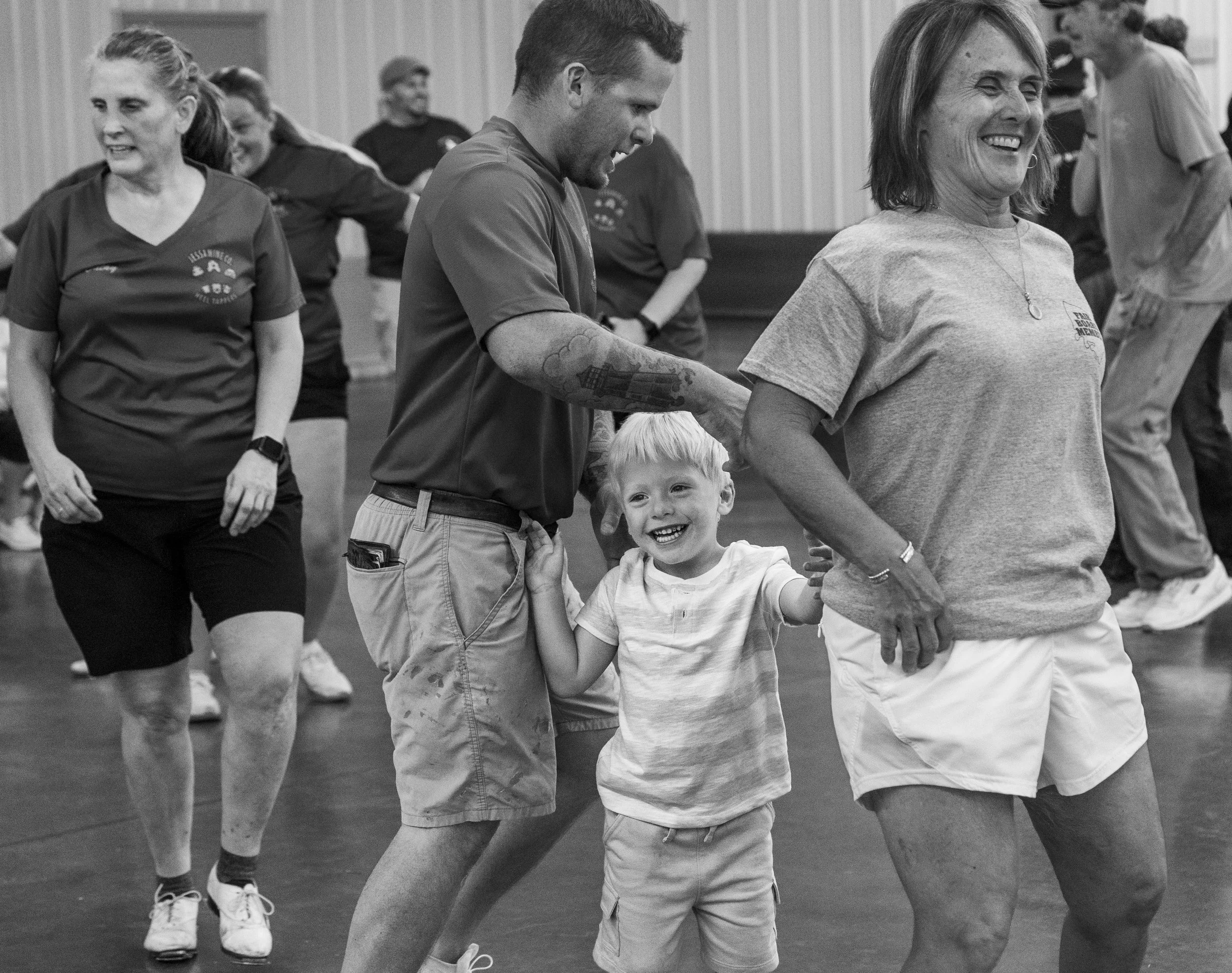 People line dancing in a gym, with a smiling young boy holding a woman's hand.