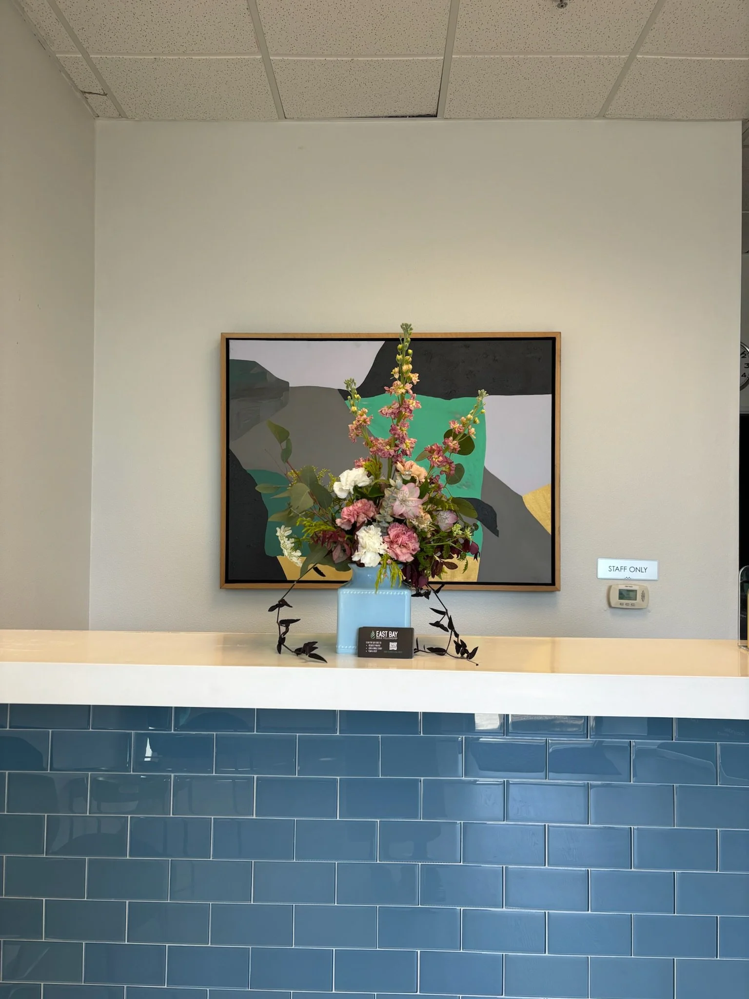 A floral arrangement of pink, white, and purple flowers on a blue vase on a reception counter with a colorful abstract painting in the background.