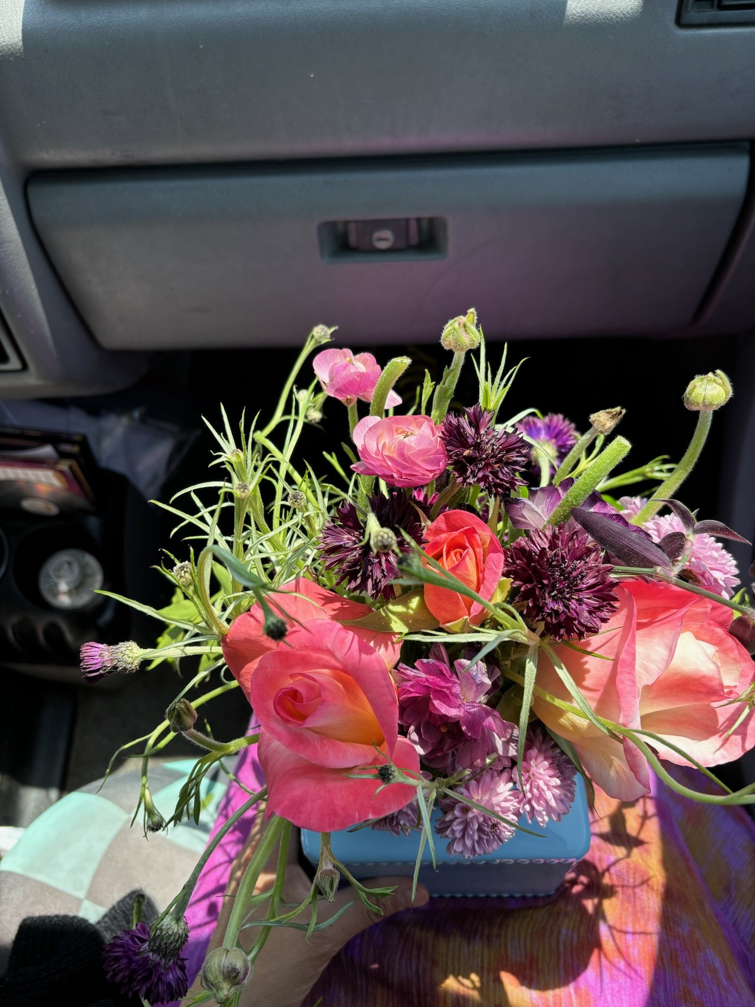 A colorful bouquet of pink, purple, and peach flowers held in a hand inside a vehicle.