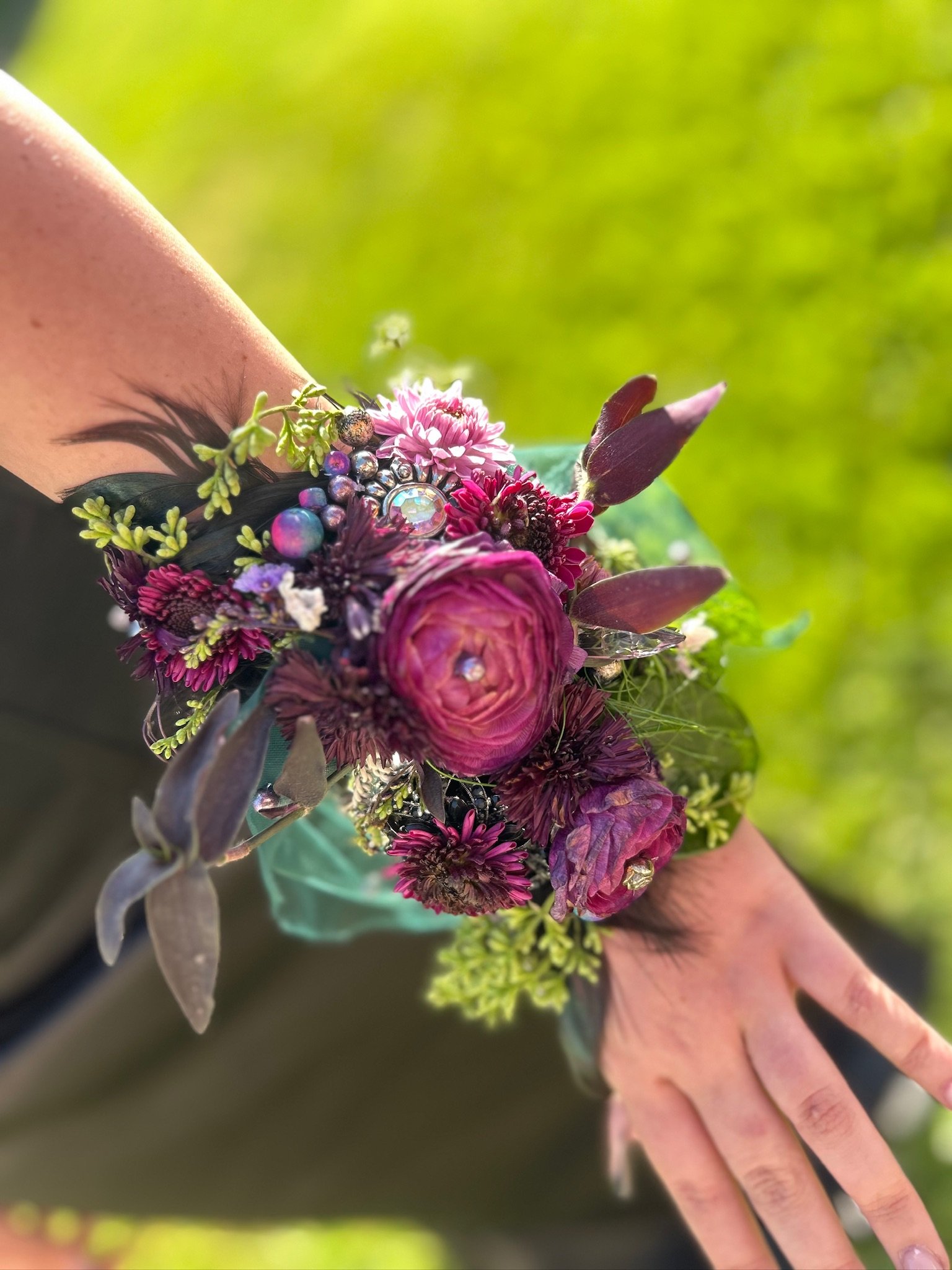Close-up of a person's wrist adorned with a dark purple and pink floral bracelet, with a green background.