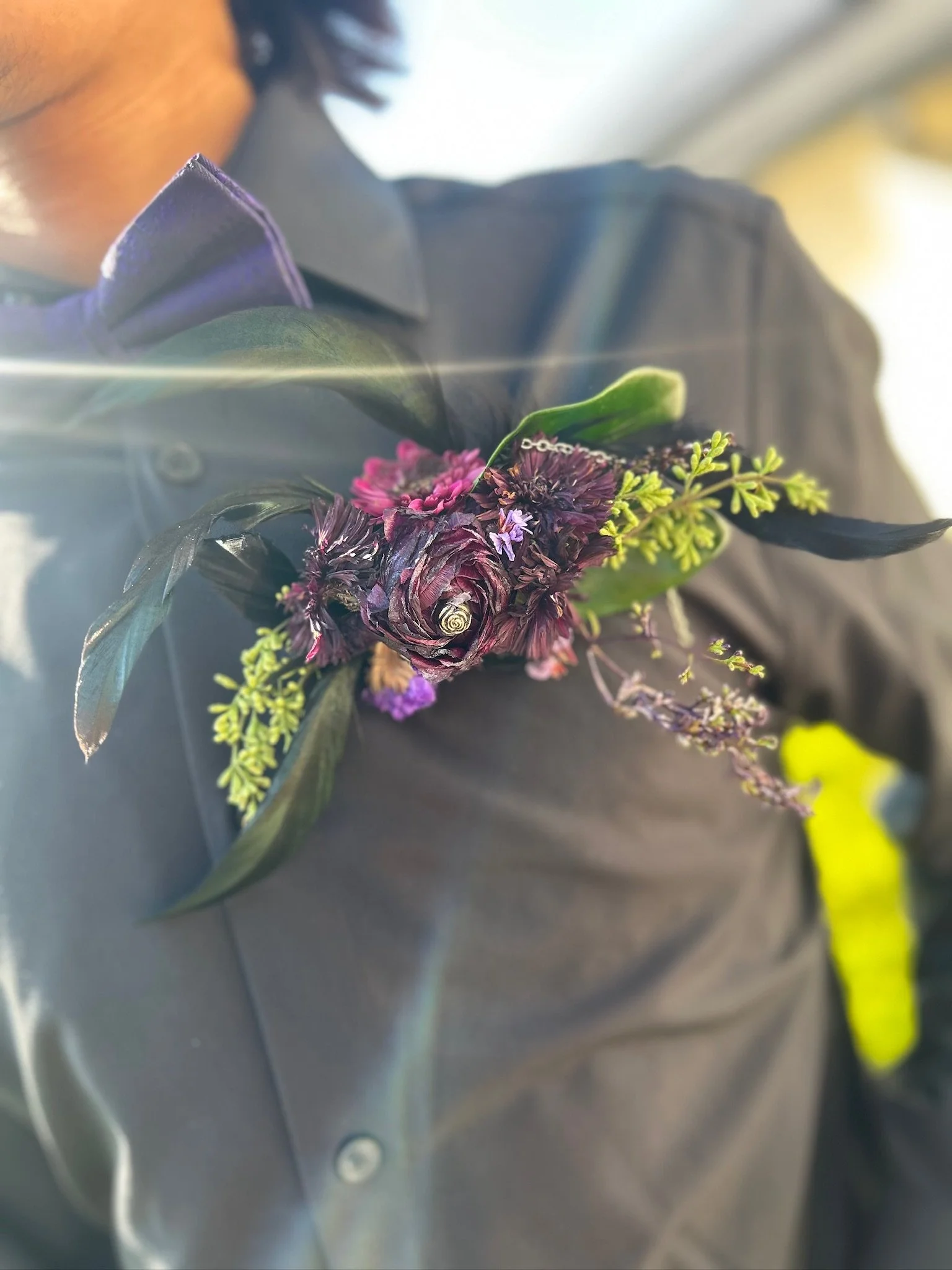 Person wearing a black shirt with a purple flower boutonniere on the lapel.