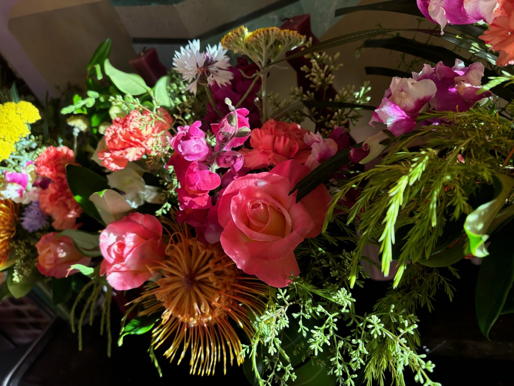 A colorful bouquet of various flowers including pink roses, carnations, yellow cluster flowers, purple and pink blossoms, and greenery.