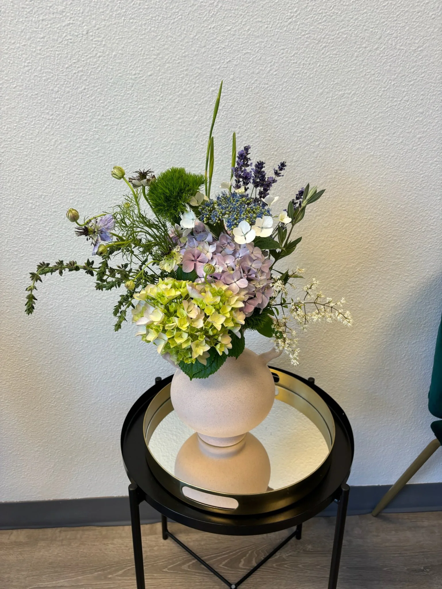 A floral arrangement with white, purple, and yellow flowers in a beige vase on a black round side table with a mirror top