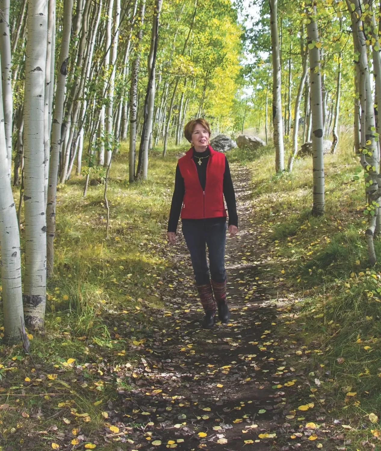 Photo of Rosalind walking on a trail surrounded by tall aspen trees with yellow and green leaves in a forest.