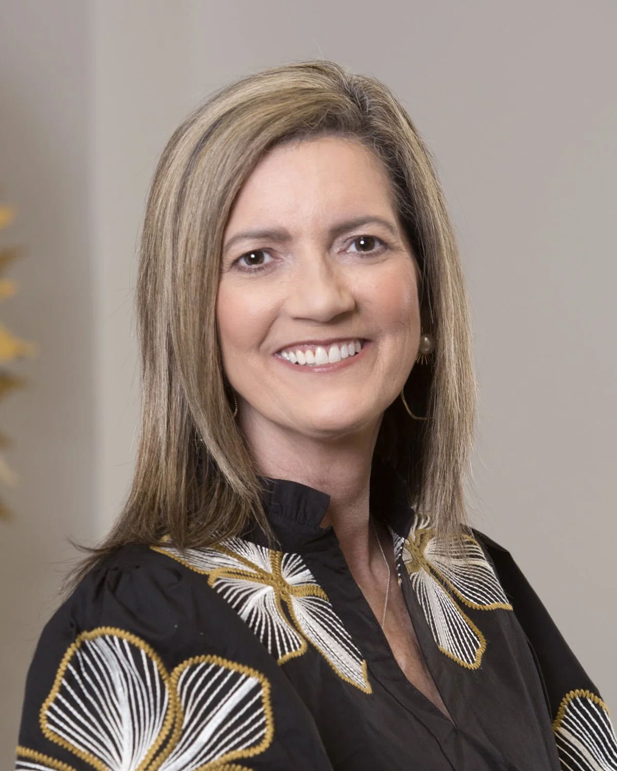 Professional woman with shoulder-length blonde hair, wearing a black blazer and white blouse, smiling in an office setting.