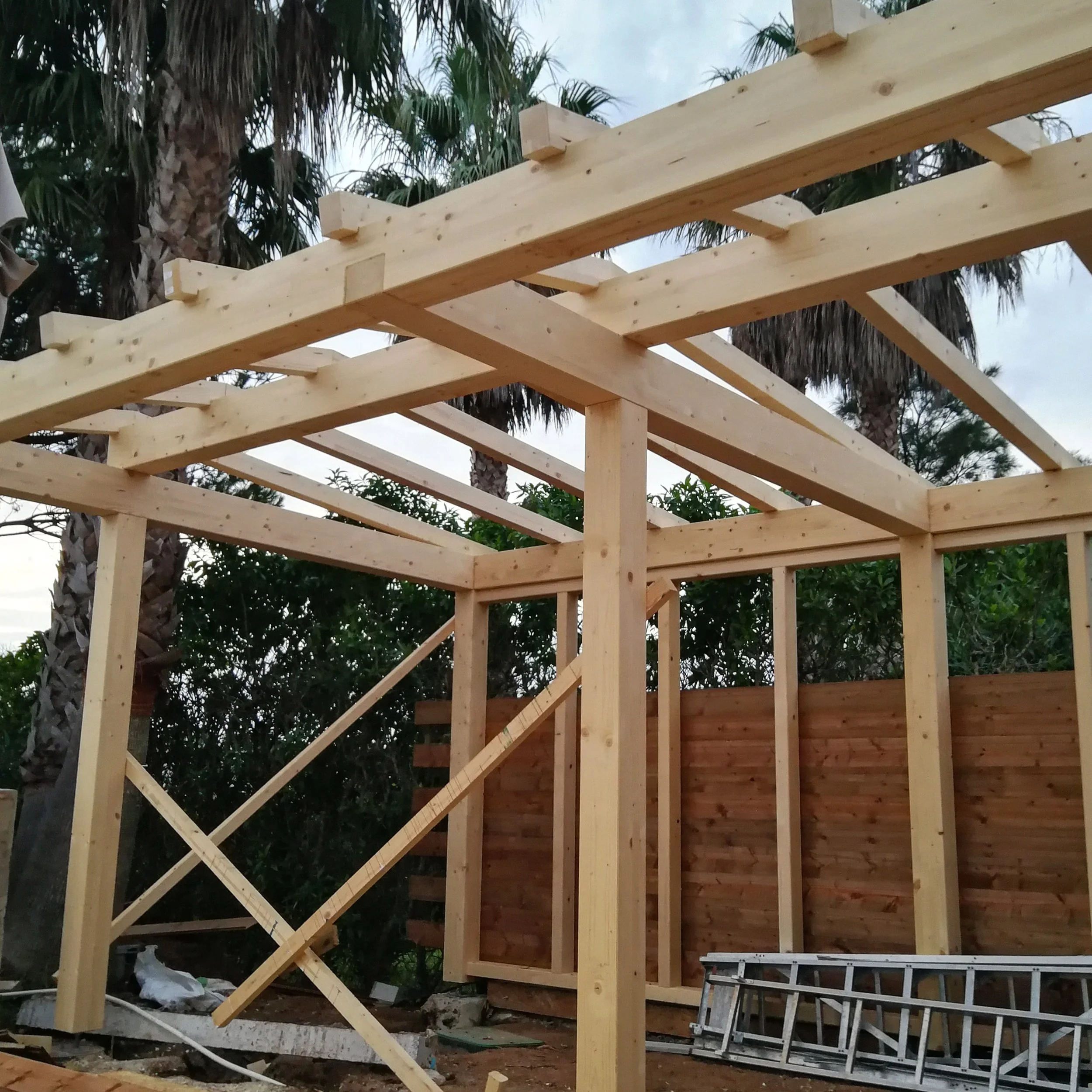 Wooden framing of a building under construction with palm trees in the background.