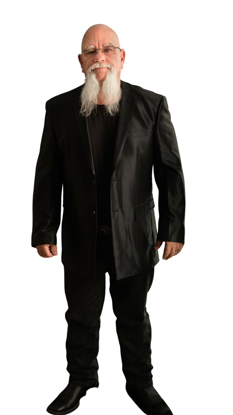 A bald man with a white beard and glasses, wearing a black leather jacket, black shirt, black pants, and black shoes. He is standing against a black background.