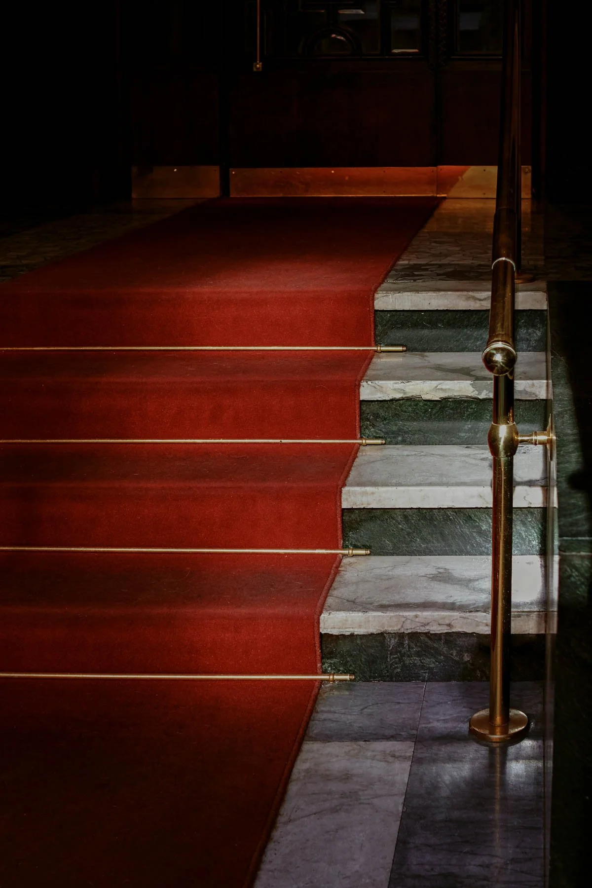 A staircase with a red carpet and a brass handrail leading up to a dark wooden door.