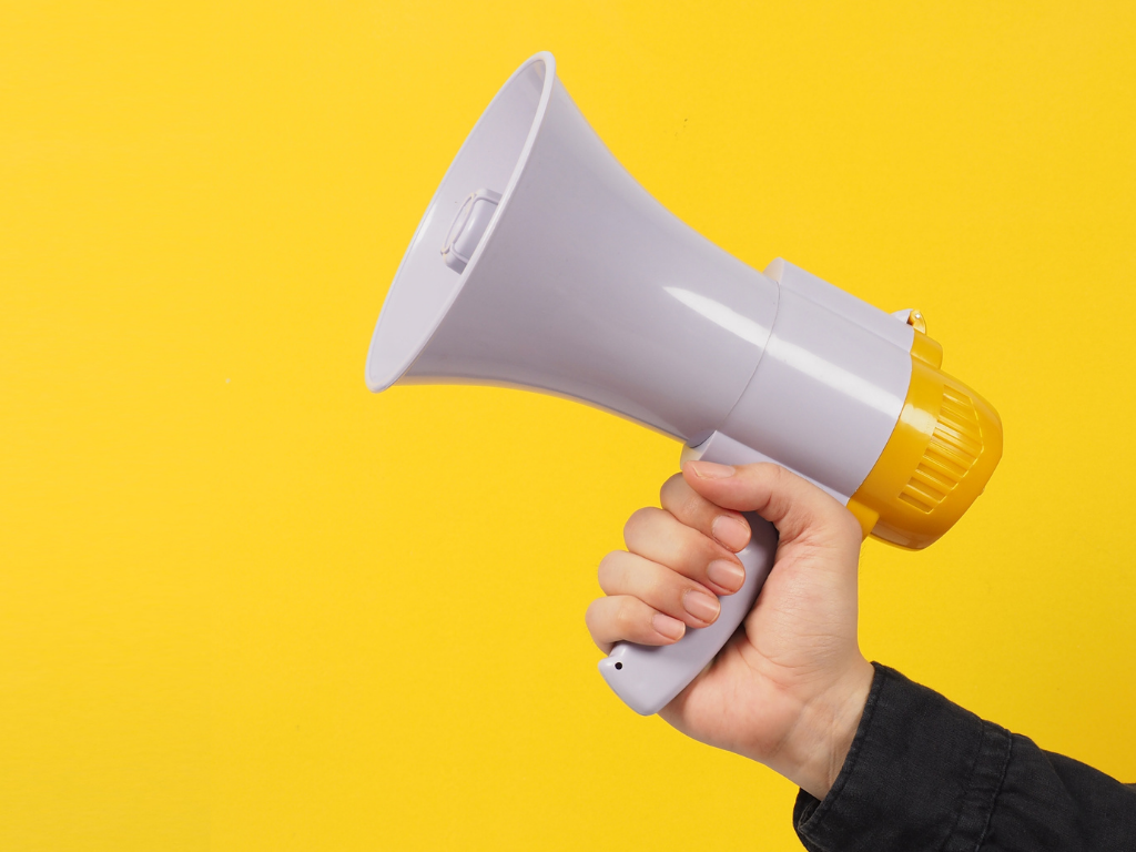 Hand holding a white megaphone with yellow accents against a yellow background.