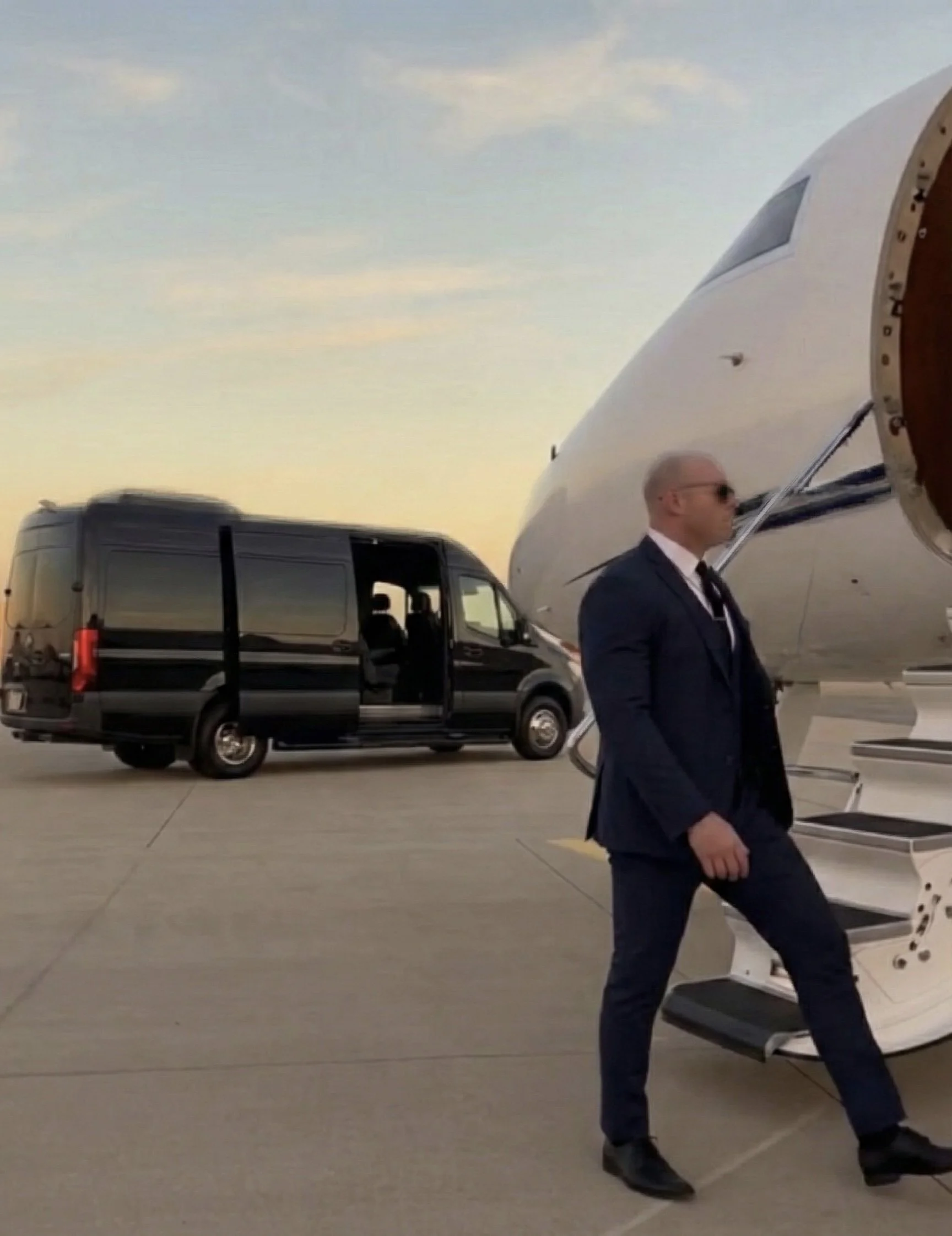 Elite Security | Private Protection. Ret. CMPD Sgt. Jonathan Steppe in a blue suit walking through a parking lot with vehicles and loading docks in an industrial area