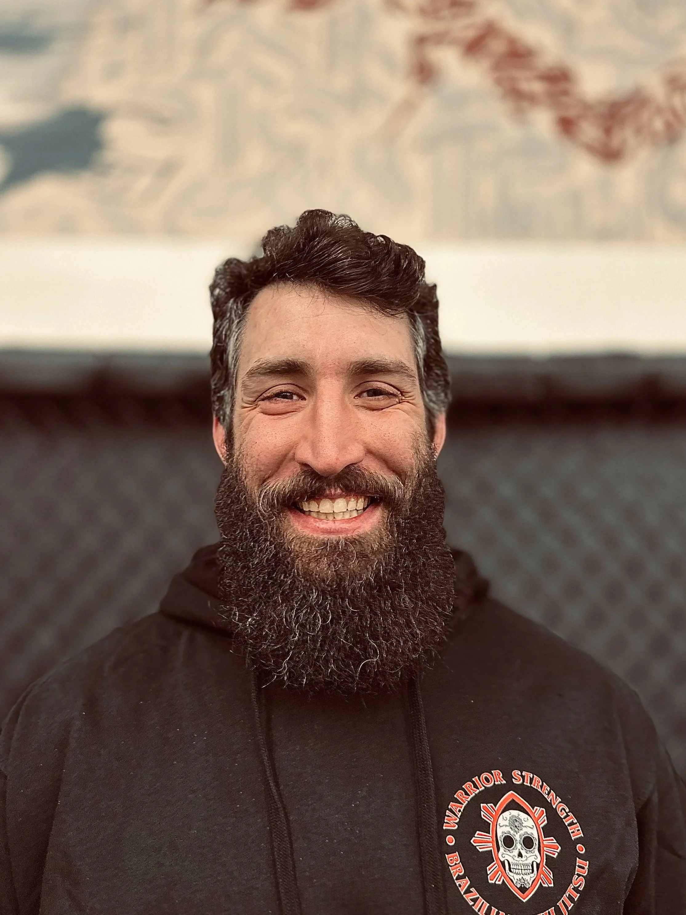 Person with a beard wearing a black WSOA shirt in a dimly lit room, possibly a workshop, with blurred background.
