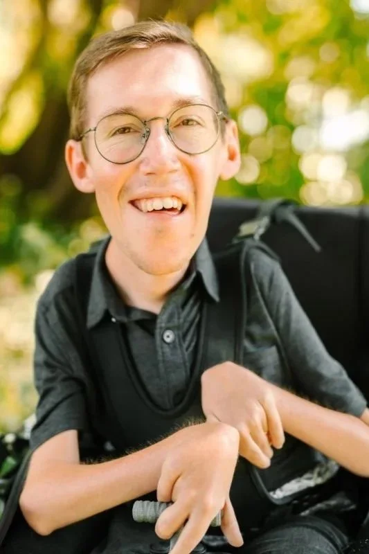 Smiling young man with glasses outdoors, carrying a backpack.