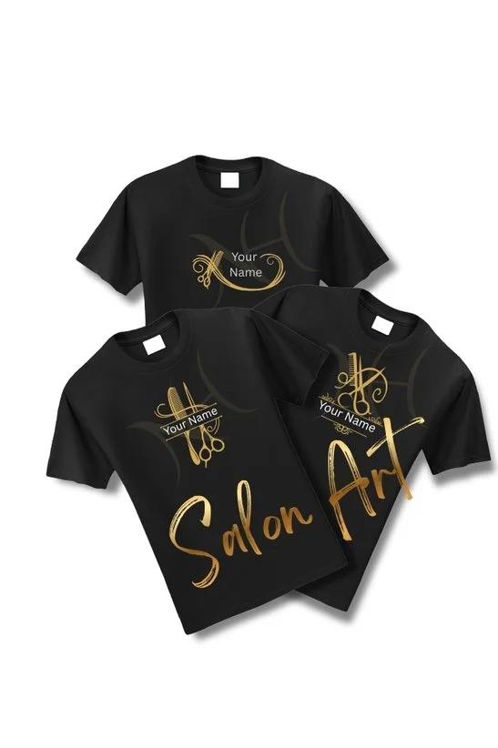 Three black T-shirts with gold-colored salon and art-themed designs, including scissors, combs, and decorative lettering, laid overlapping on a plain background.