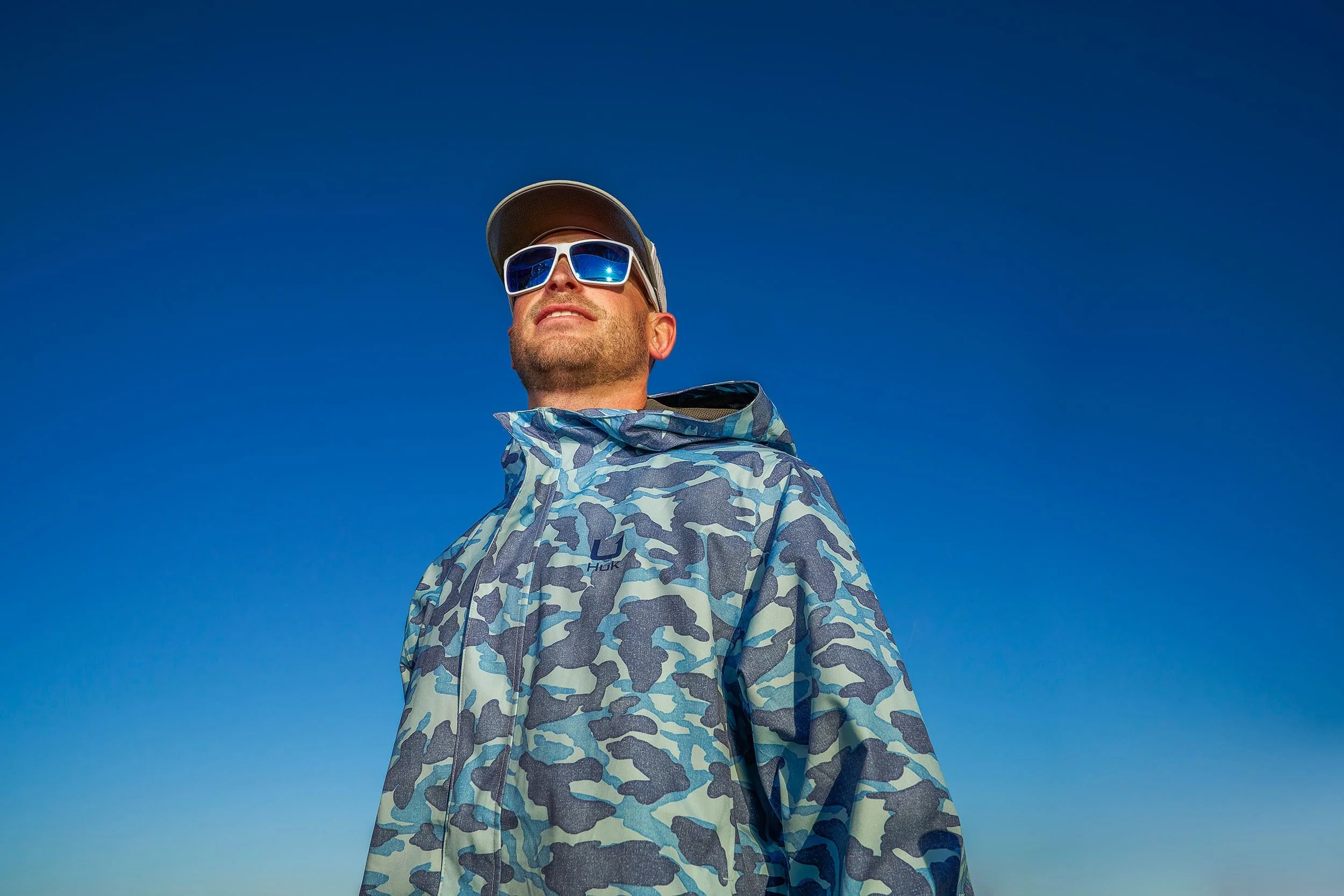 HUK fishing apparel portrait of man in camo jacket and sunglasses against blue sky in Cabo San Lucas, outdoor lifestyle photography