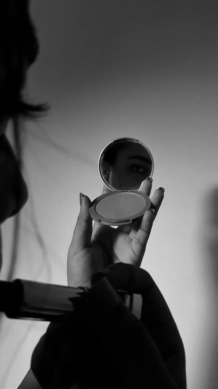 Woman in a robe getting makeup applied, smiling with closed eyes.
