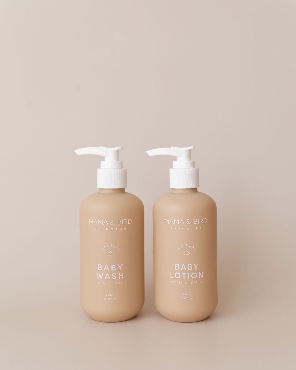 Two beige bottles of Mama & Bird skincare for babies, labeled Baby Wash and Baby Lotion with pump dispensers, placed on a neutral background.