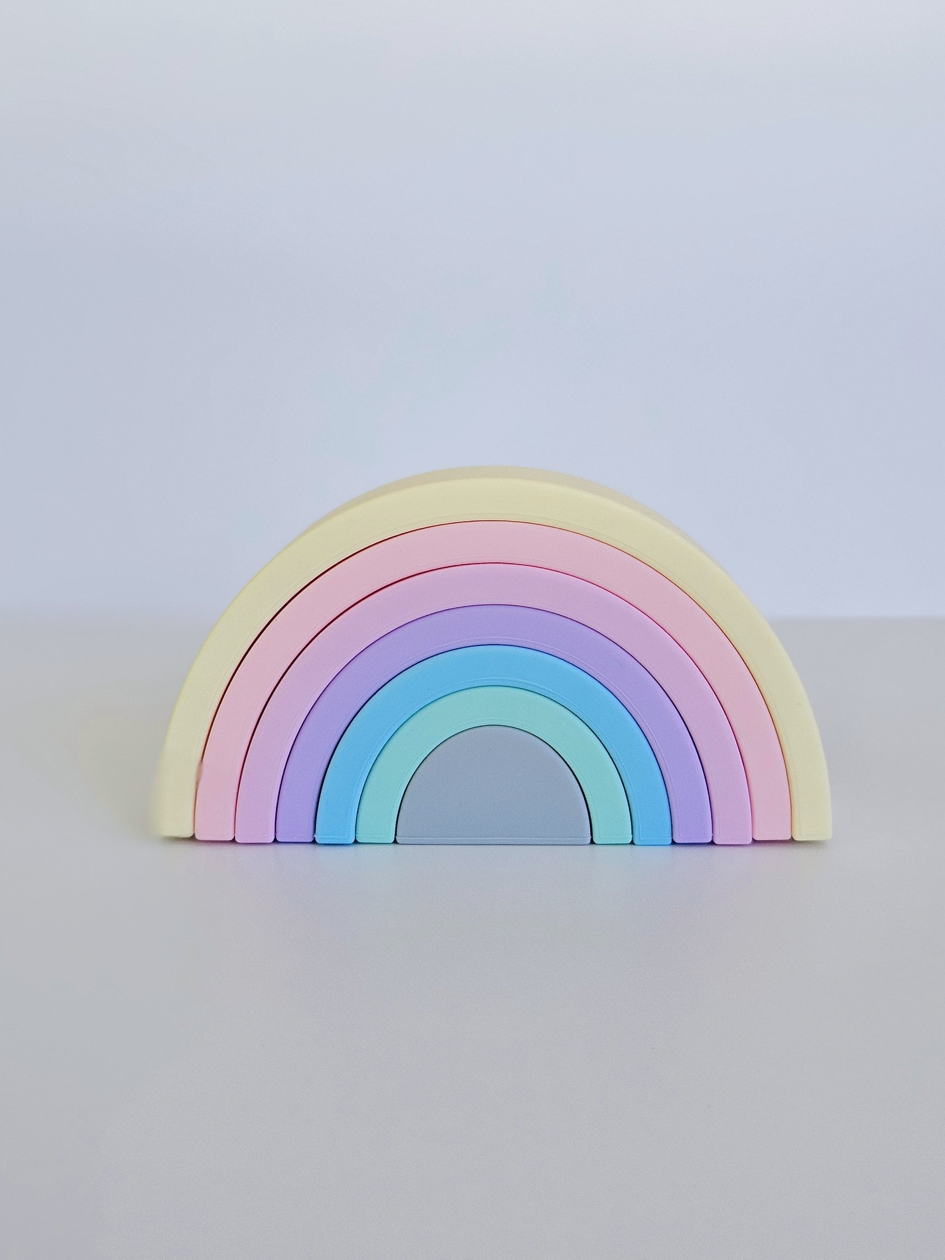 A pastel-colored rainbow with six arches in soft shades of yellow, pink, purple, blue, and teal, set against a neutral background.