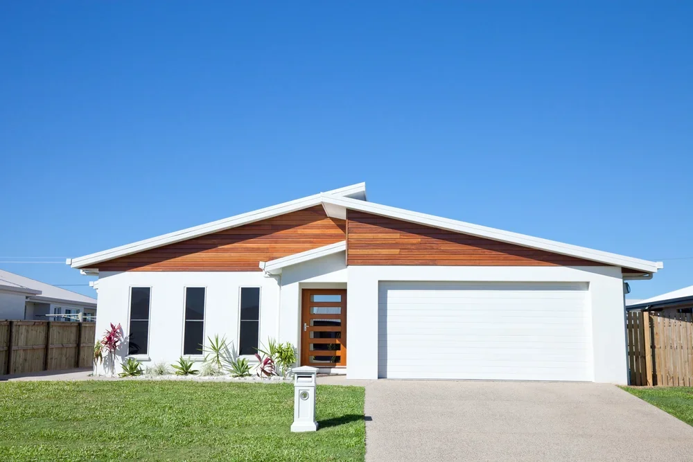 Single-story white residential home exterior featuring warm timber gable accents and a double garage