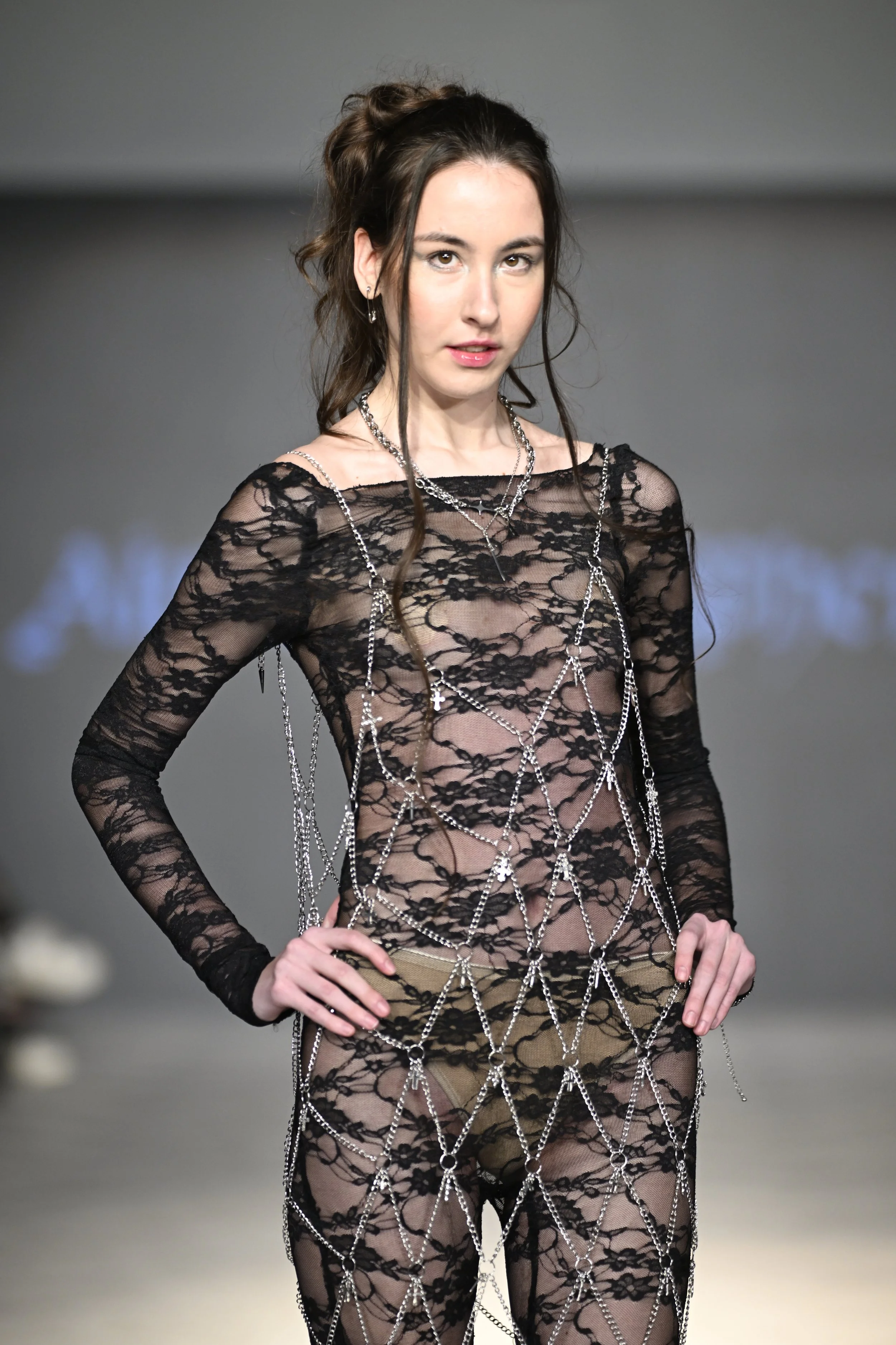 Olena wears a sheer lace, low back catsuit, overlayed with a midi length chain dress with charms.