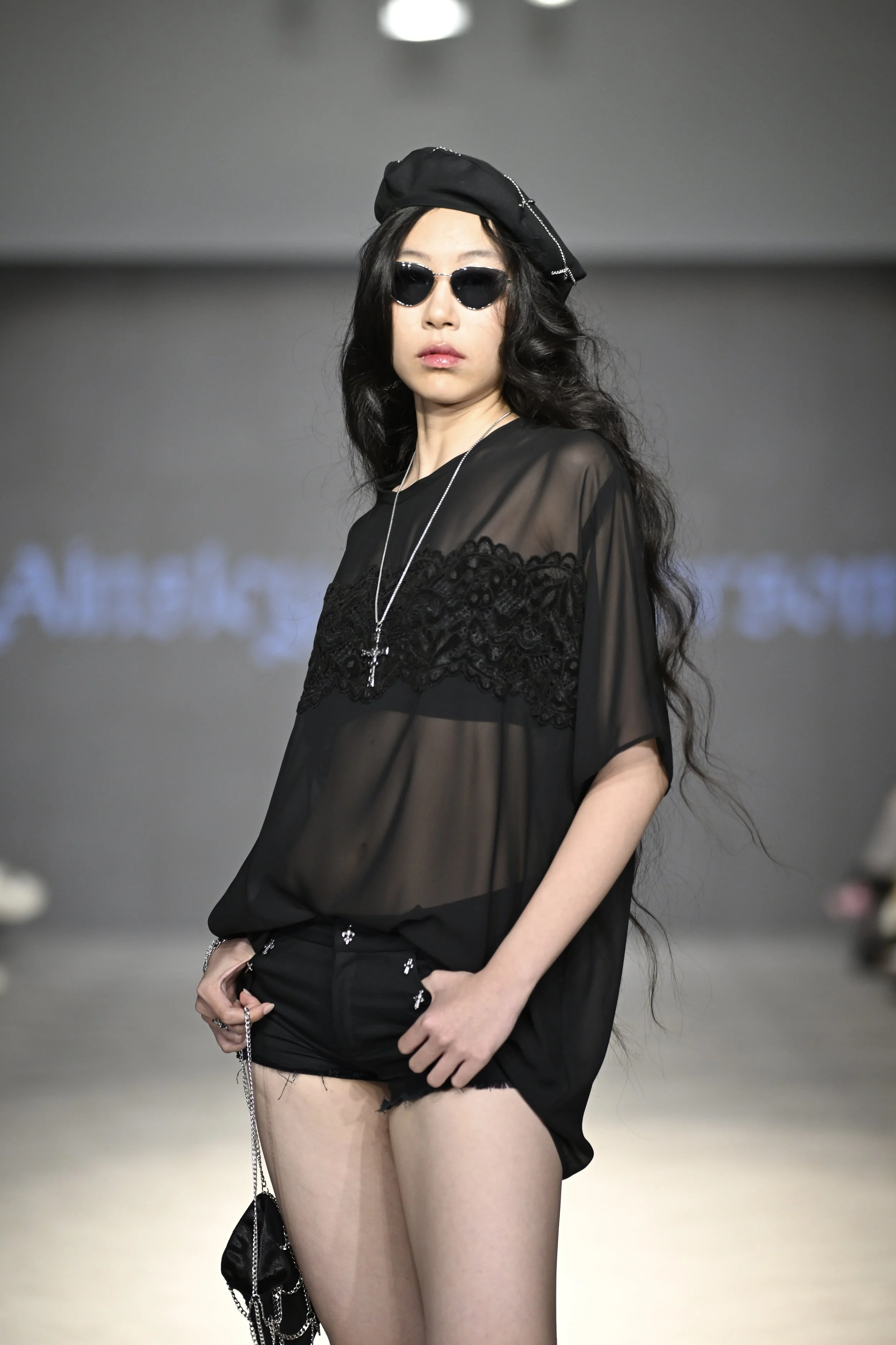 Iris wears a sheer chiffon oversized tee with lace appliqué and distressed denim micro shorts with charm detailing. She wears a chain detailed beret and co-ord mini bag.