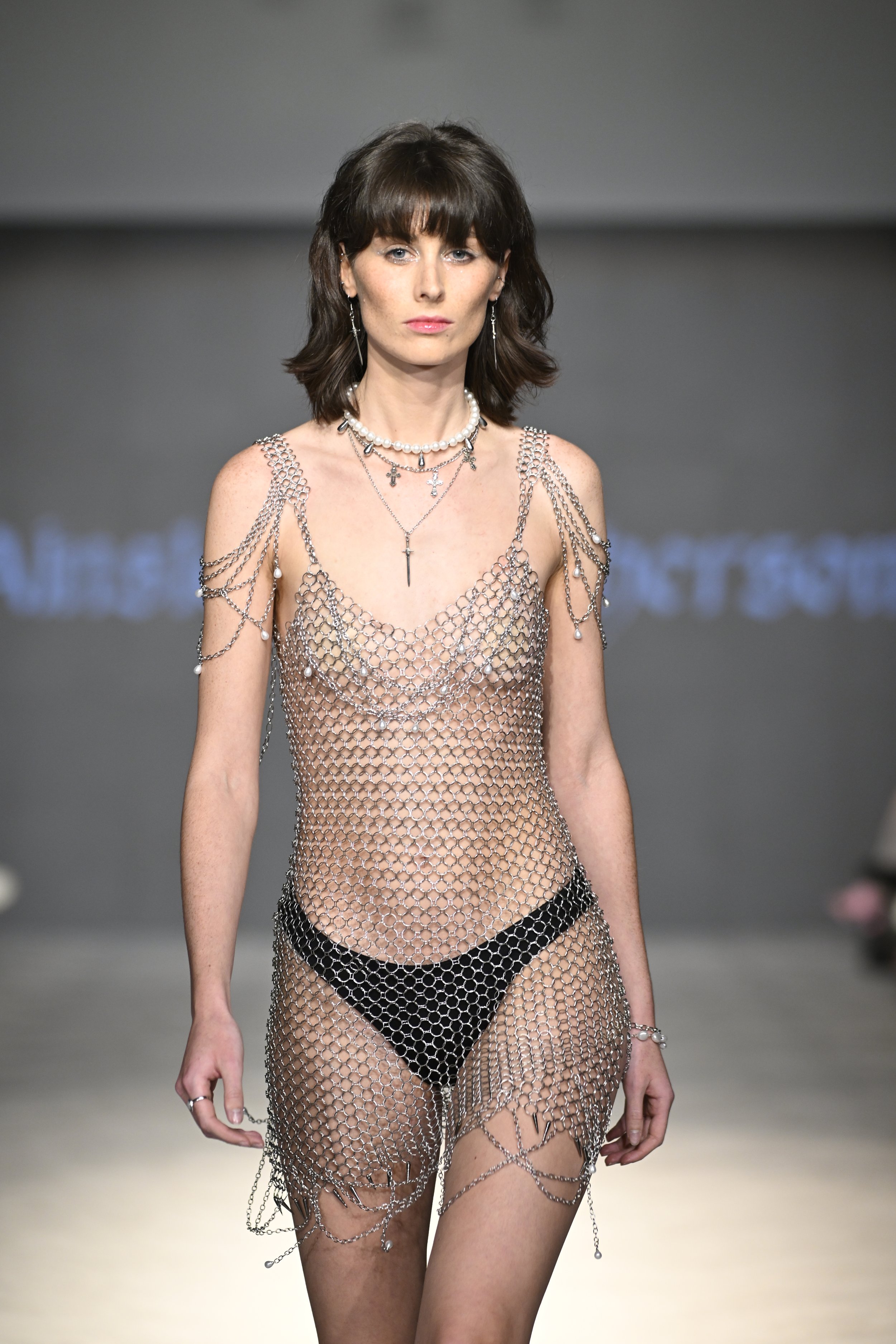 Kerri wears a handmade chainmail slip dress with pearl and chain detailing, including off shoulder draped epaulette accents.