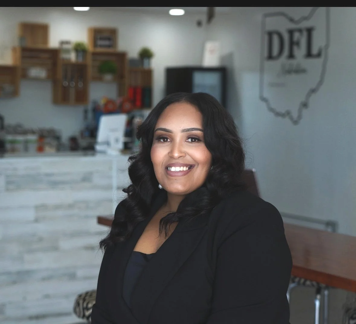 Smiling woman in a business suit in an office setting with a decorative wall in the background.