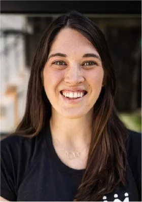 A smiling woman with long brown hair wearing a black shirt.