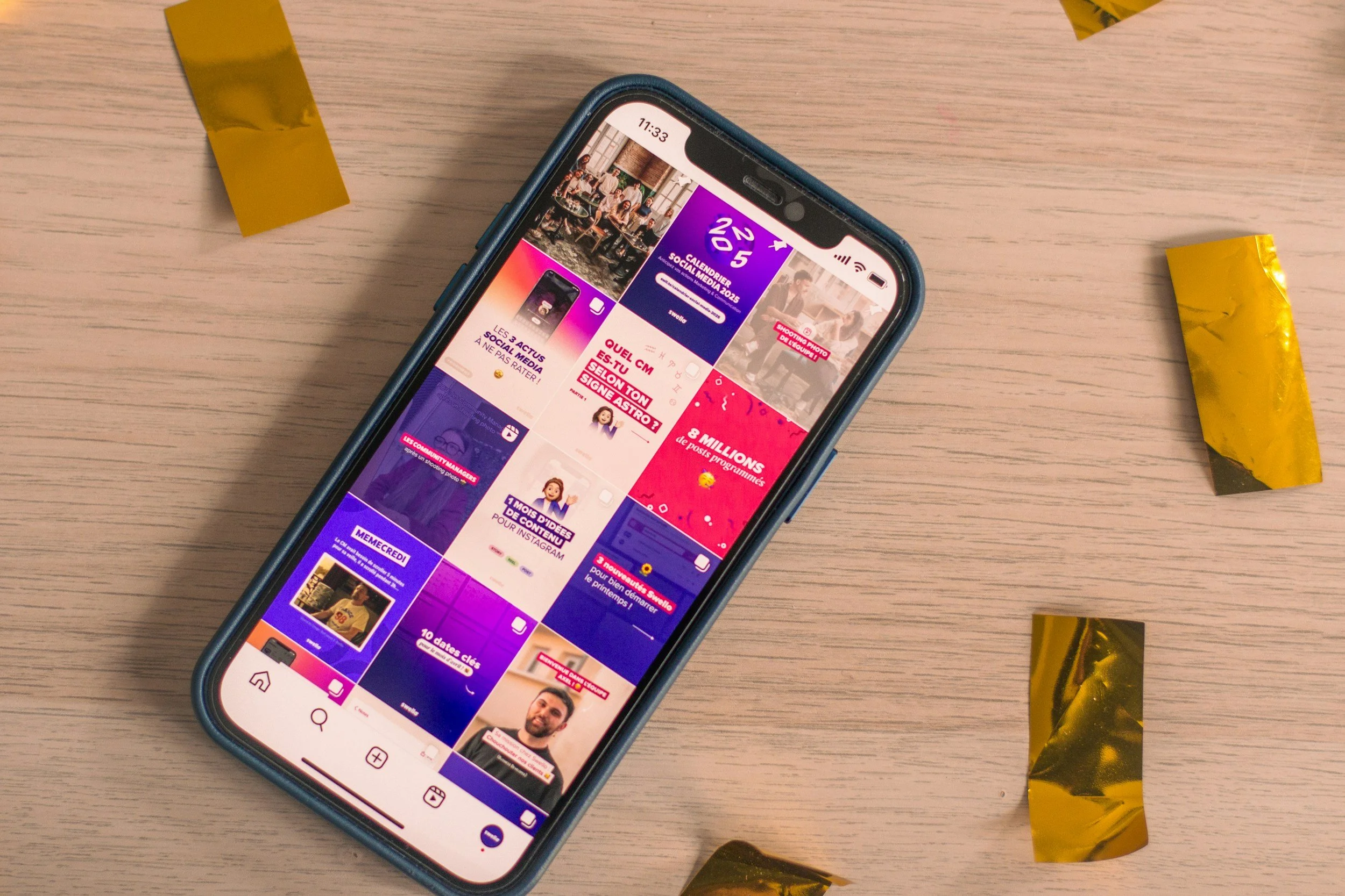 Smartphone resting on a wooden surface displaying a social media app with bright colored sections and images. Two yellow wrapped candies are partially visible, one above and one below the phone.