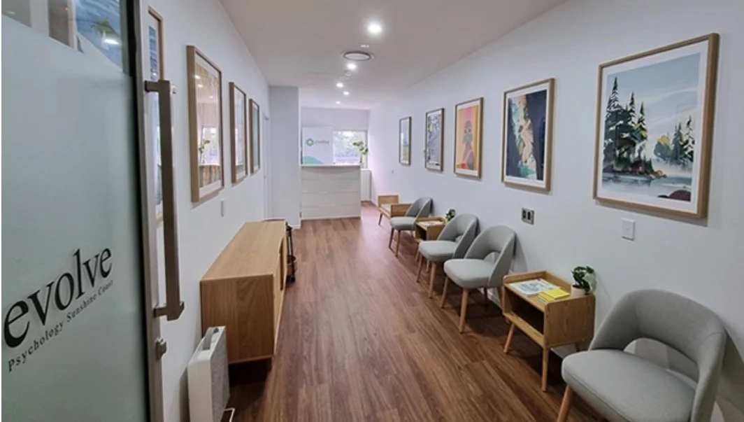 Waiting area inside a mental health clinic with modern chairs, small tables with books, and framed artwork on white walls.