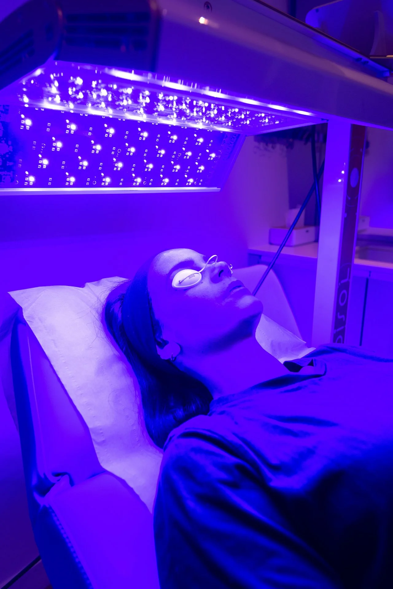 Une femme allongée sur un lit dans une salle de traitement de luminothérapie, sous une lumière LED bleue violette.