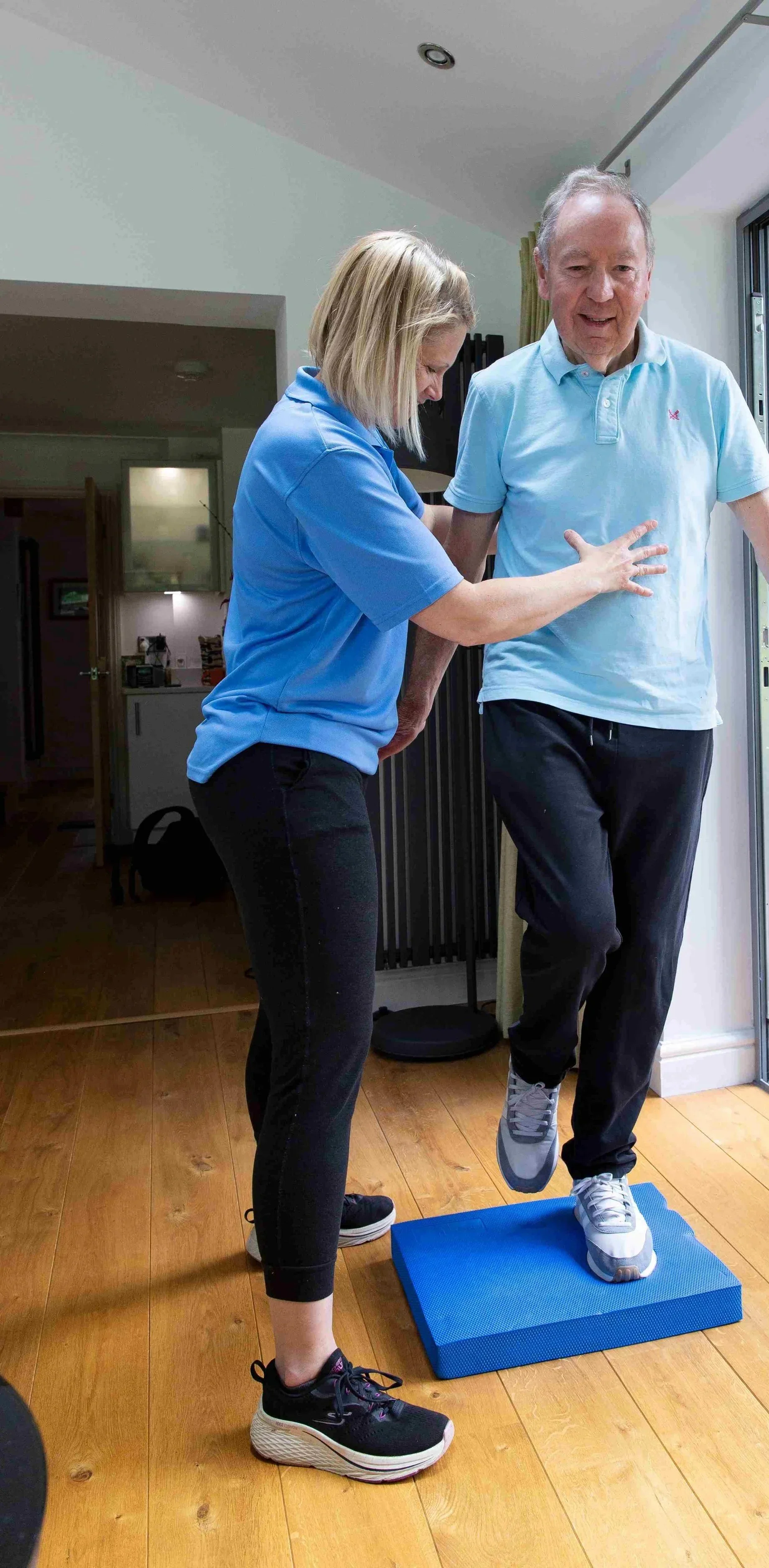 Physiotherapist helping an elderly client with balance exercises to prevent falls at home in Winchester.