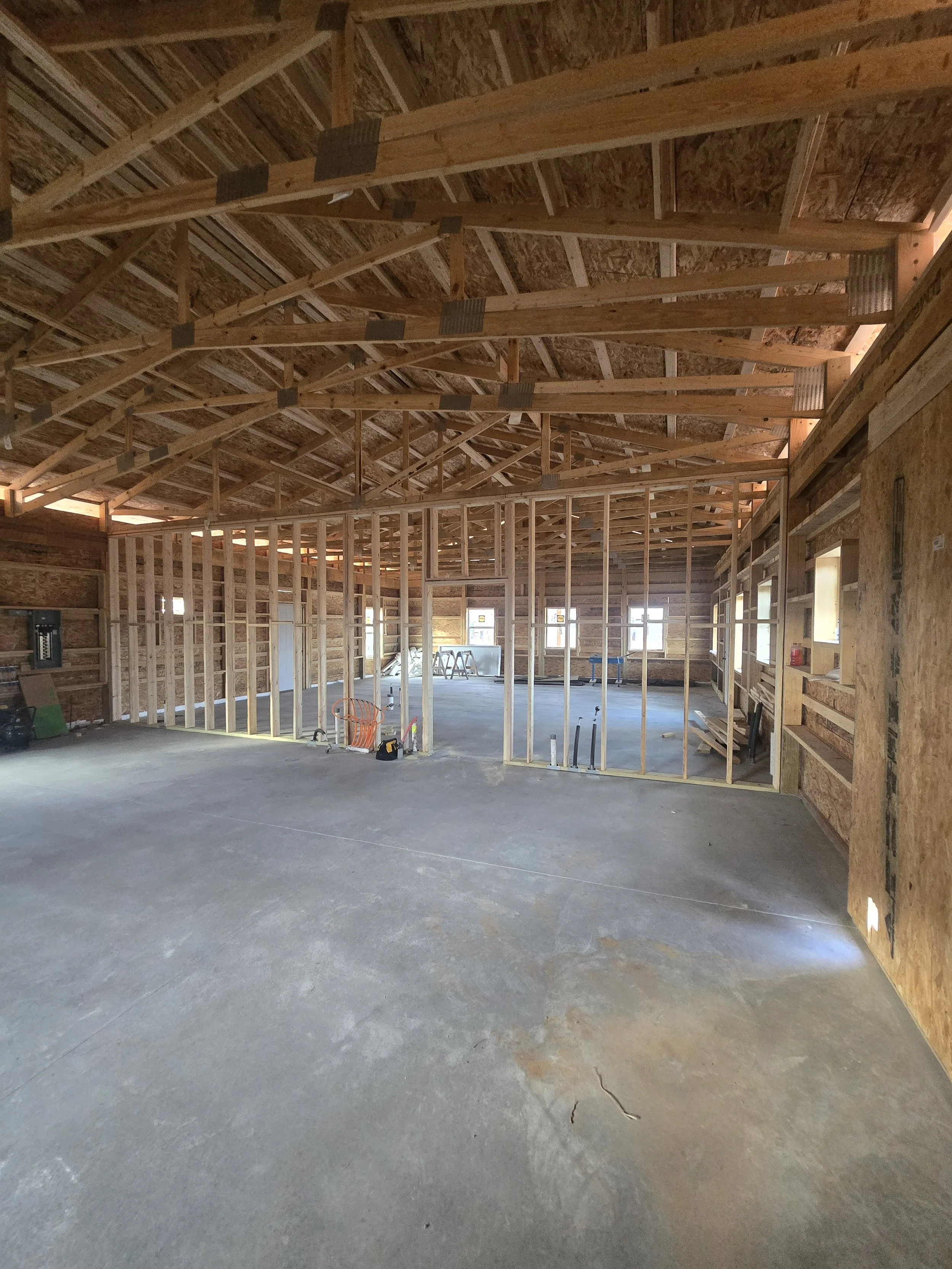 Interior view of a building under construction with exposed wooden framing, high ceiling, and concrete floor.