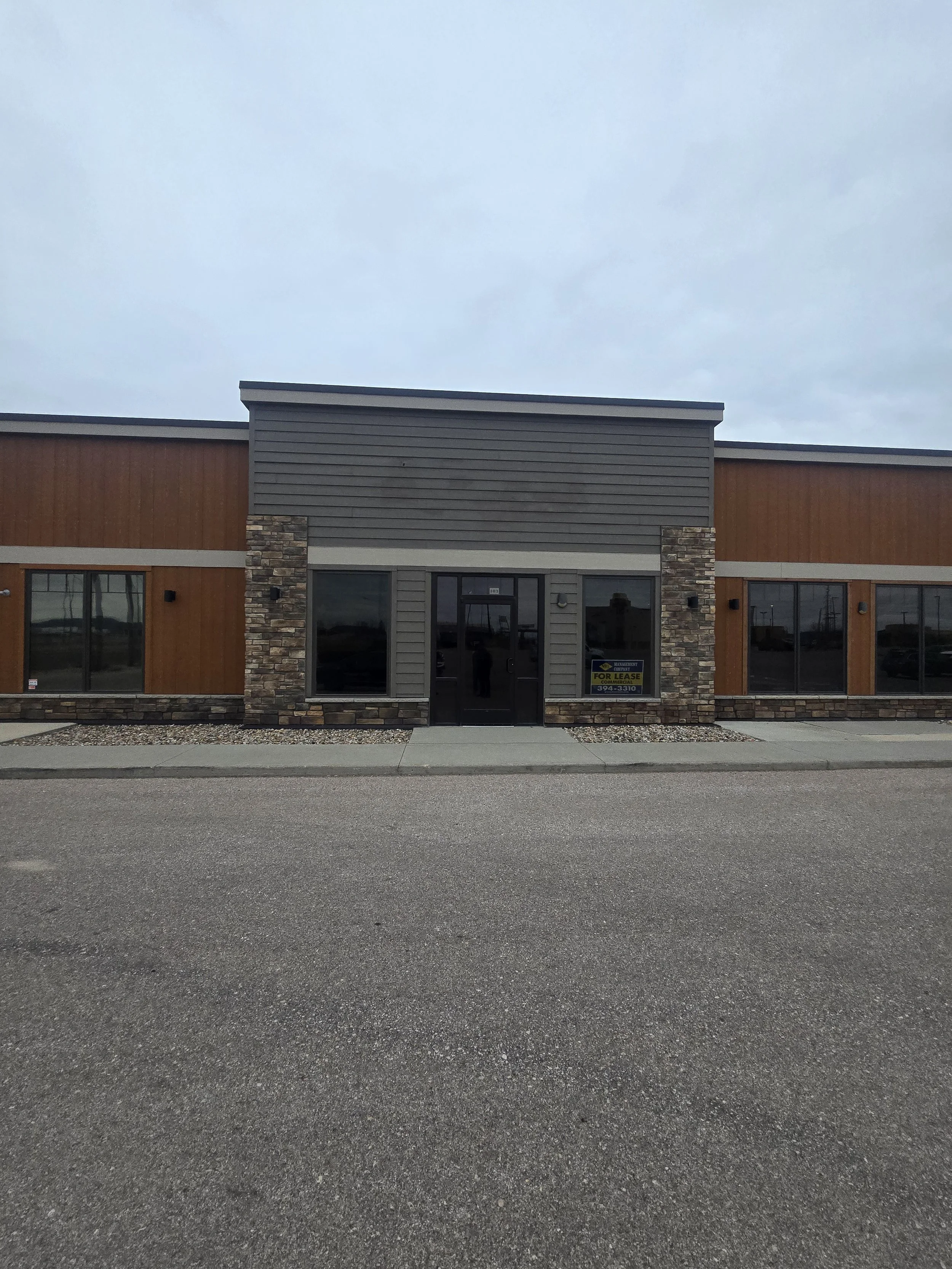 Commercial building with brick and siding exterior, large windows, and a 'For Lease' sign in the window.