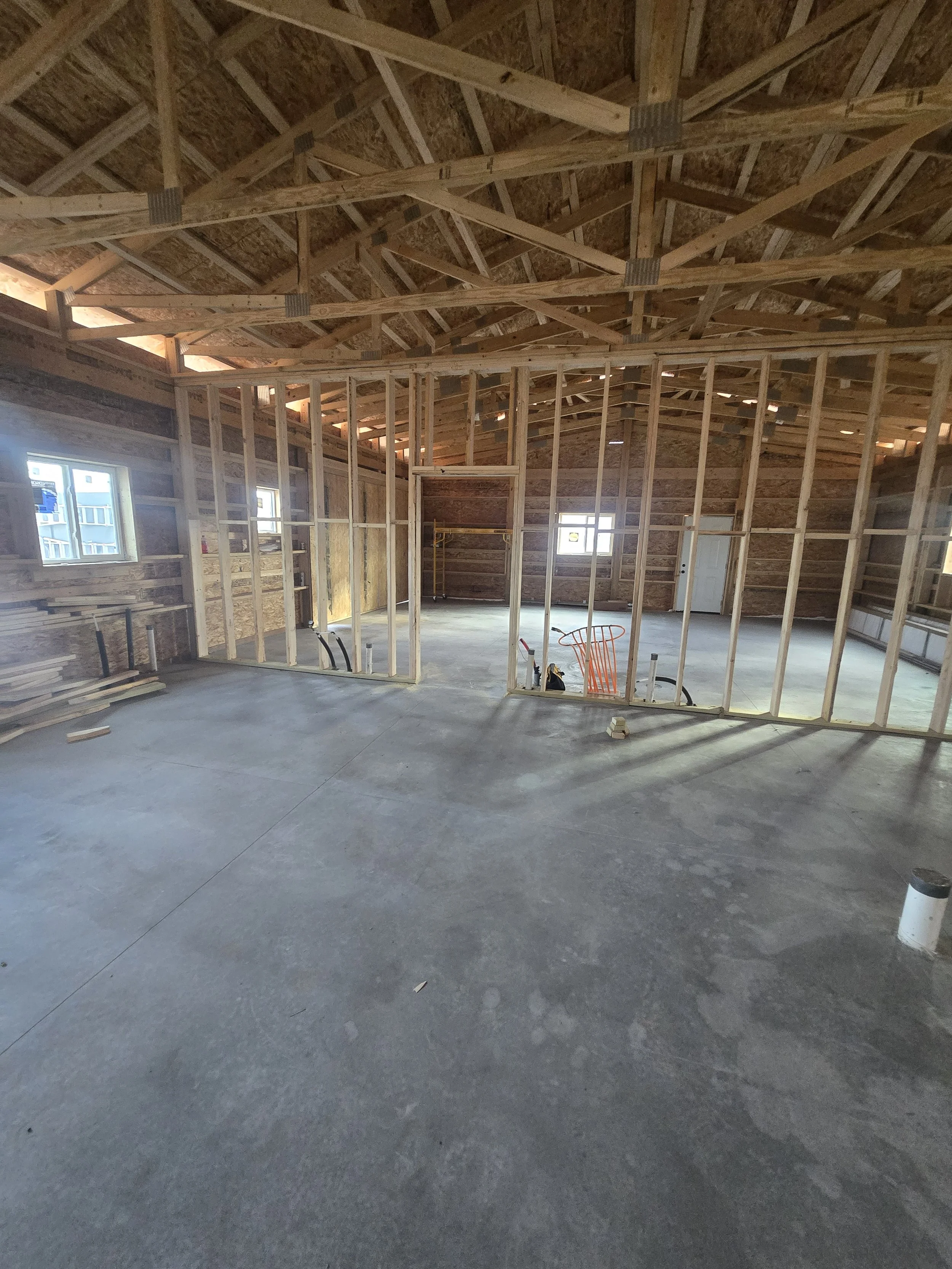 Interior of a house under construction with exposed wooden framing, new windows, and a concrete floor.