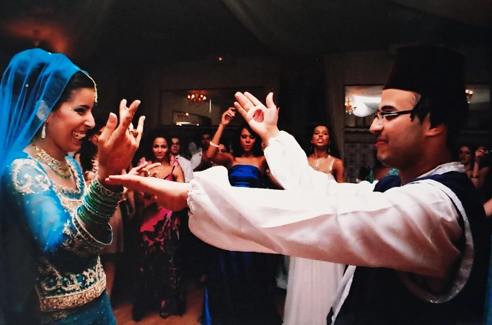 Un homme et une femme en tenue traditionnelle indienne dansant lors d'une cérémonie, entourés d'autres personnes en soirée.