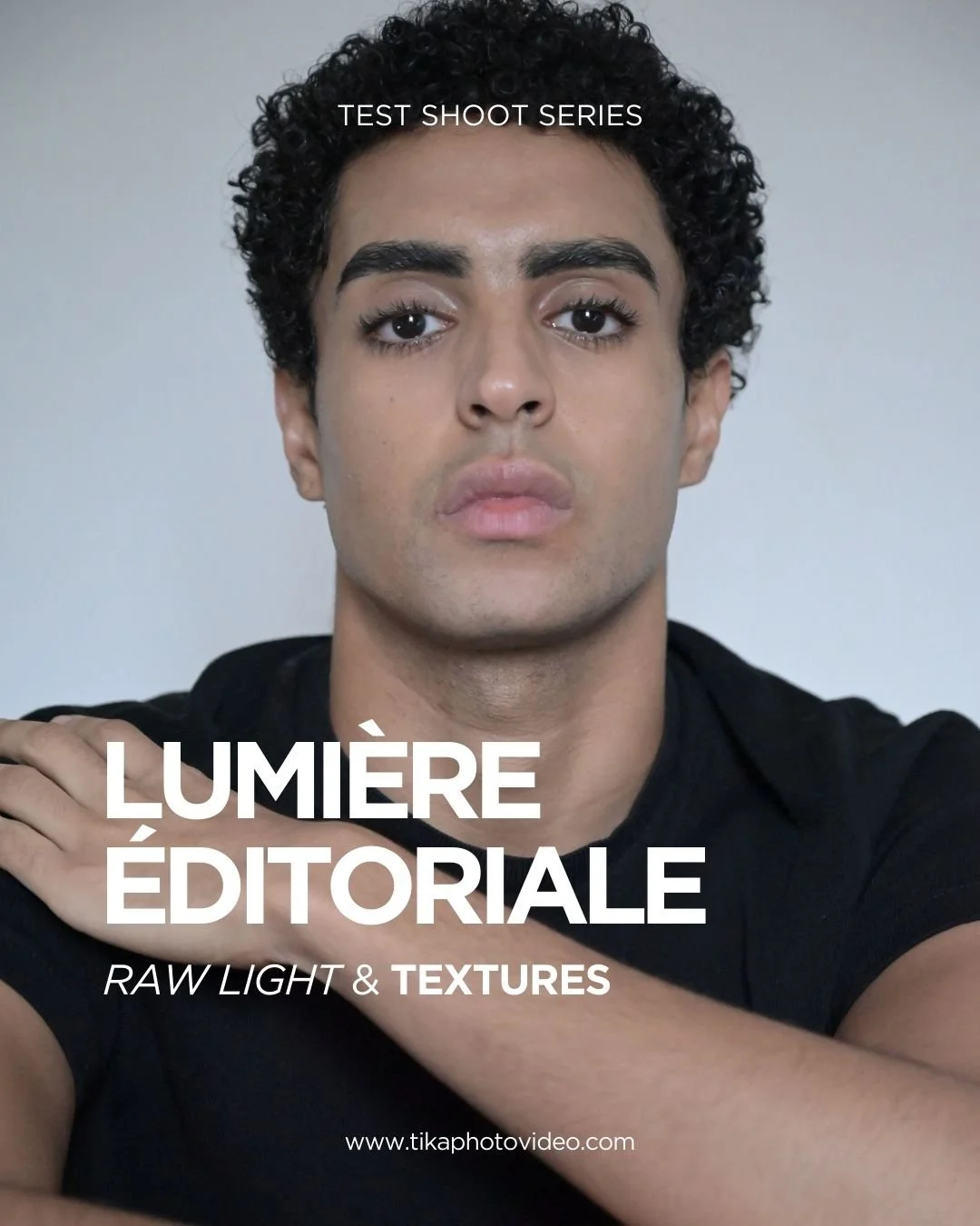 Un New Face avec des cheveux bouclés noirs regarde droit devant, portant un t-shirt noir, avec un fond gris clair. Texte sur l'image : "TEST SHOOT SERIES, LUMIÈRE ÉDITORIALE, RAW LIGHT & TEXTURES".