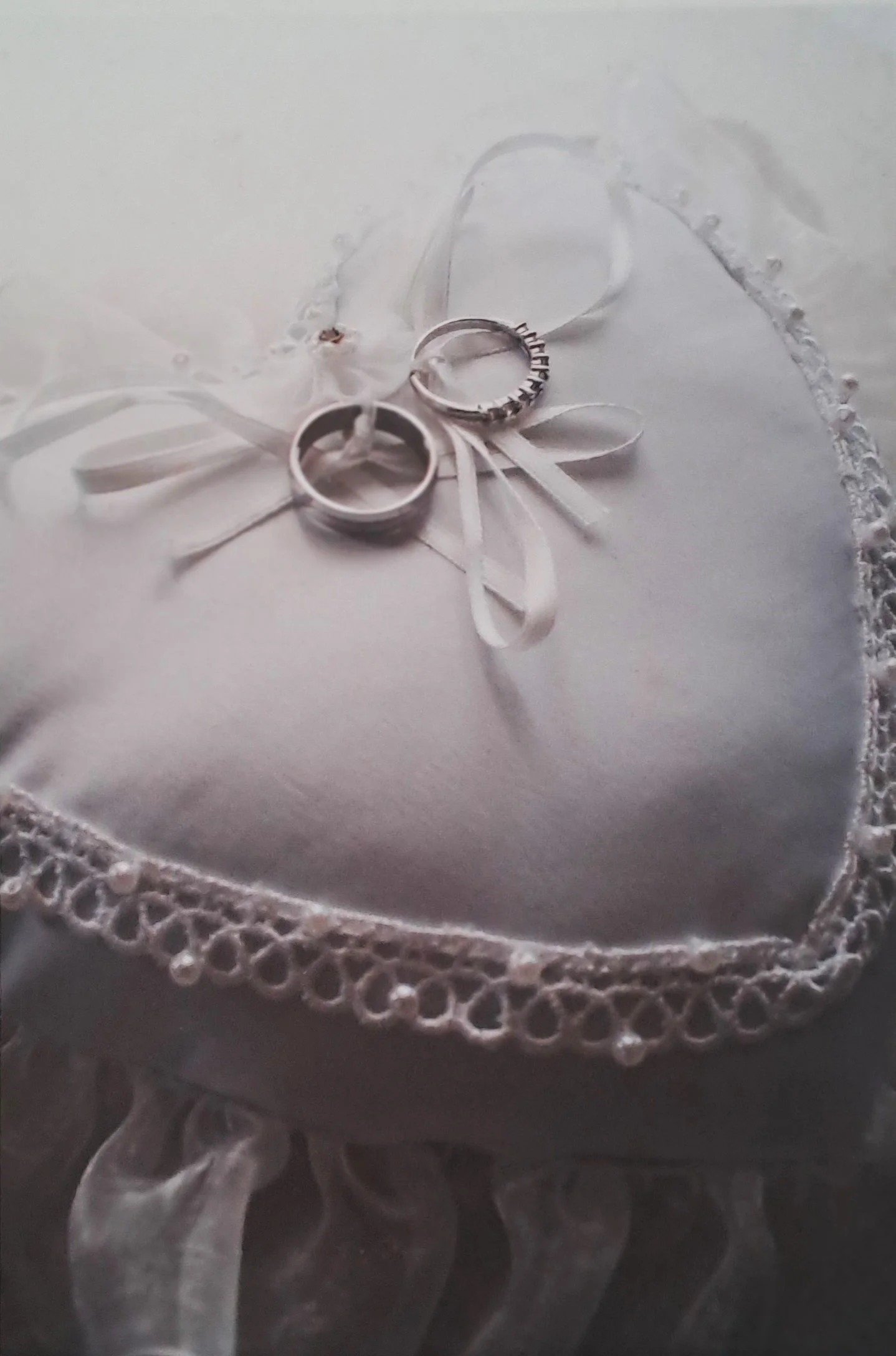 Deux alliances de mariage posées sur un coussin blanc décoré de dentelle, avec un ruban en satin blanc.