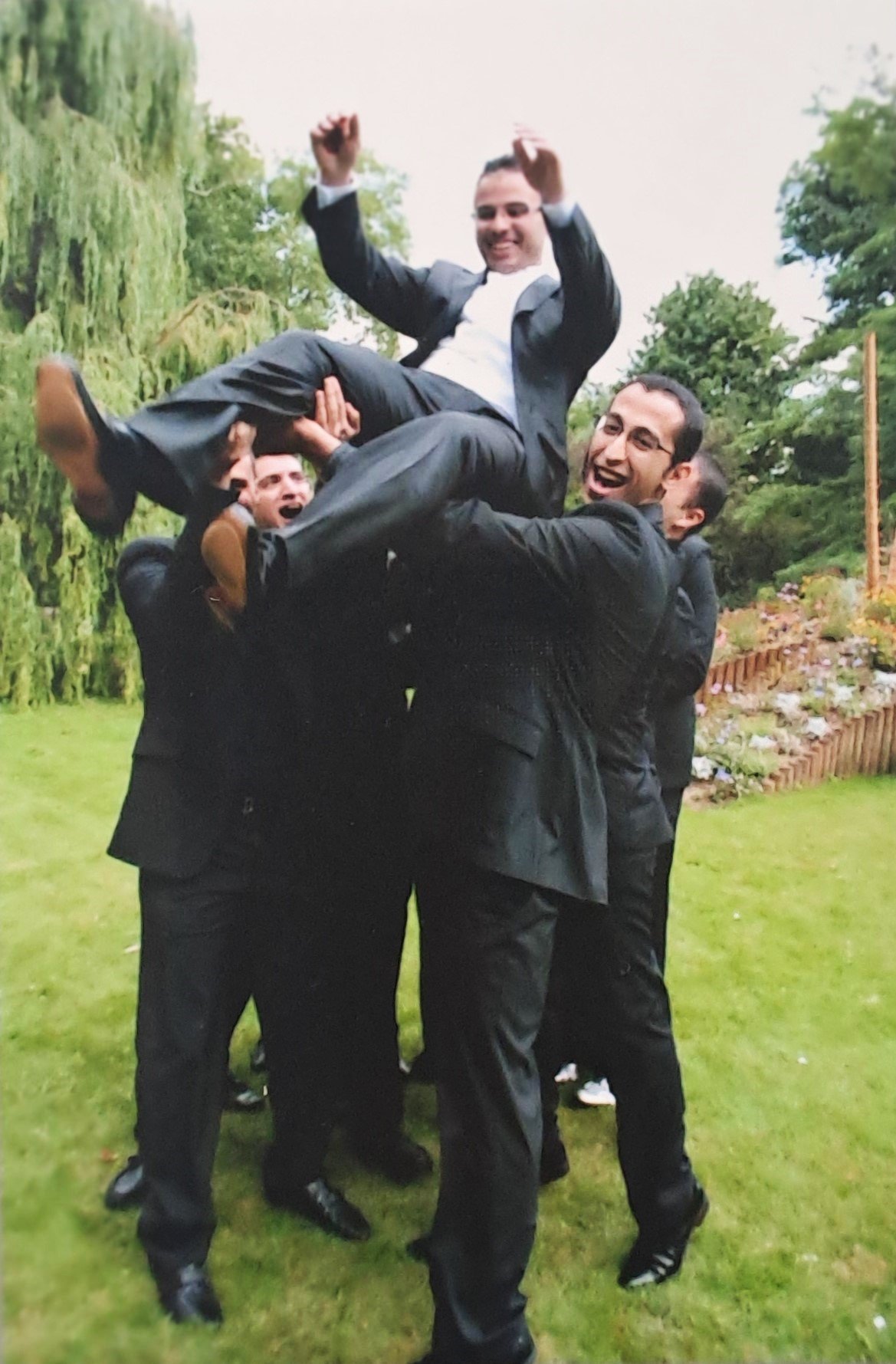 Groupe d'hommes en costumes d'affaires soulevant un homme dans un parc, tous souriant et riant.